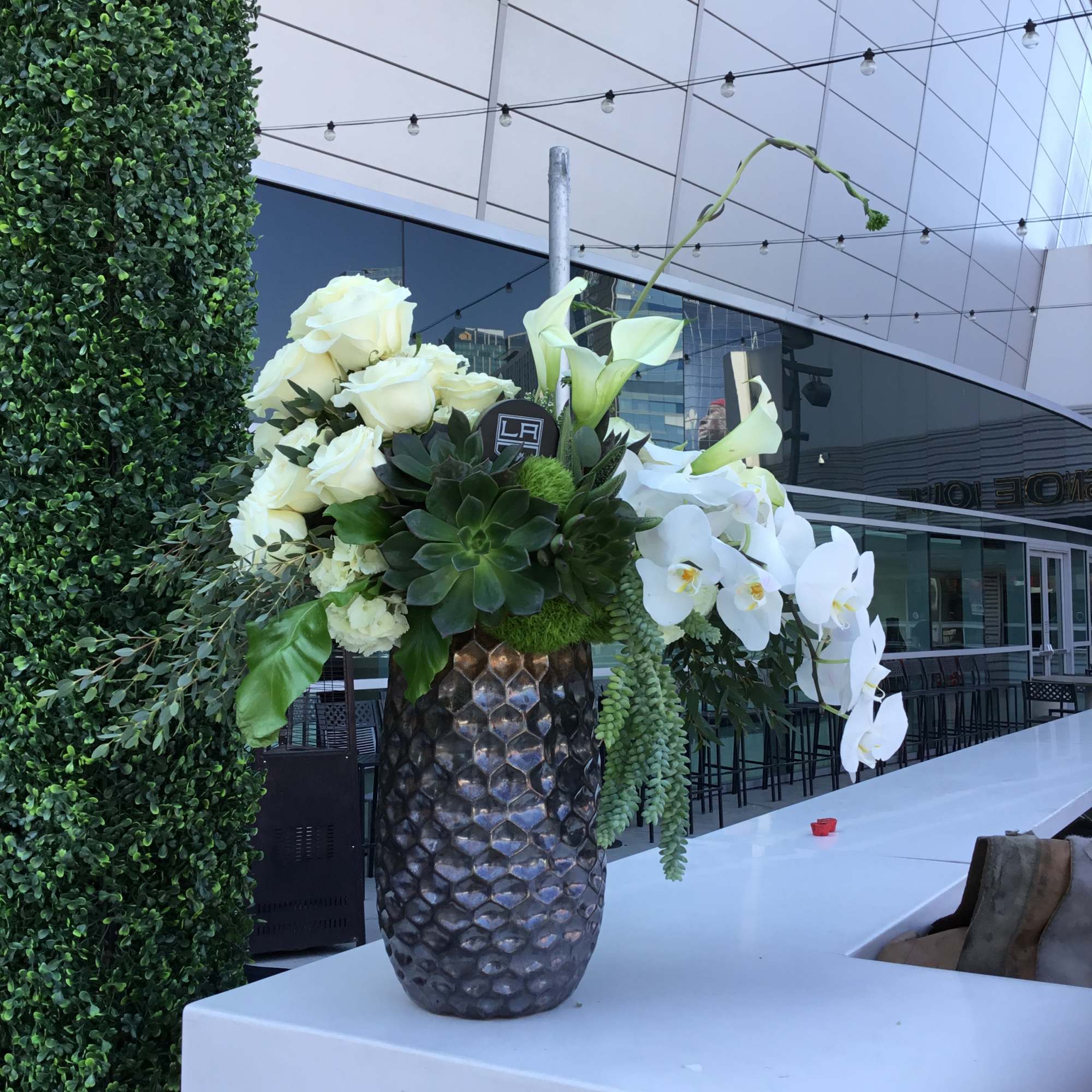 White roses and calla lilies in a textured vase with succulents