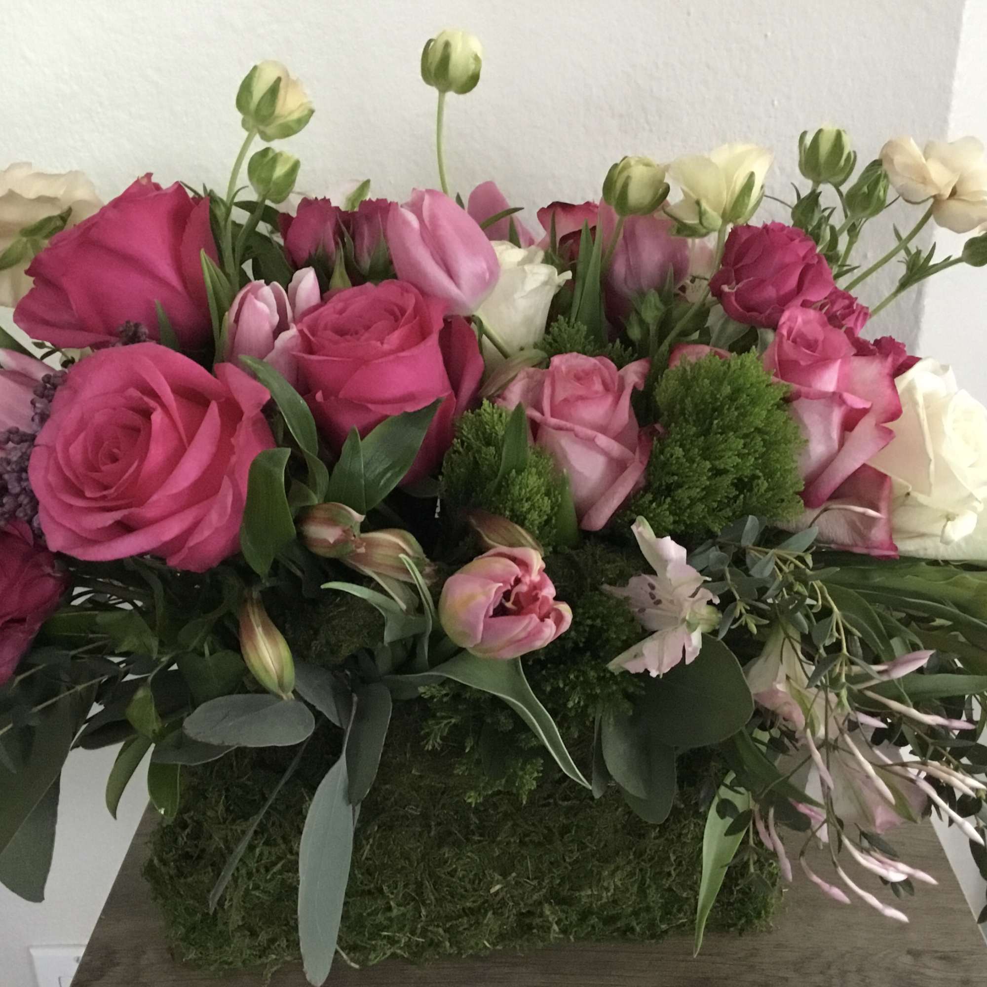 Pink and white rose bouquet with tulips and greenery in a moss-covered container