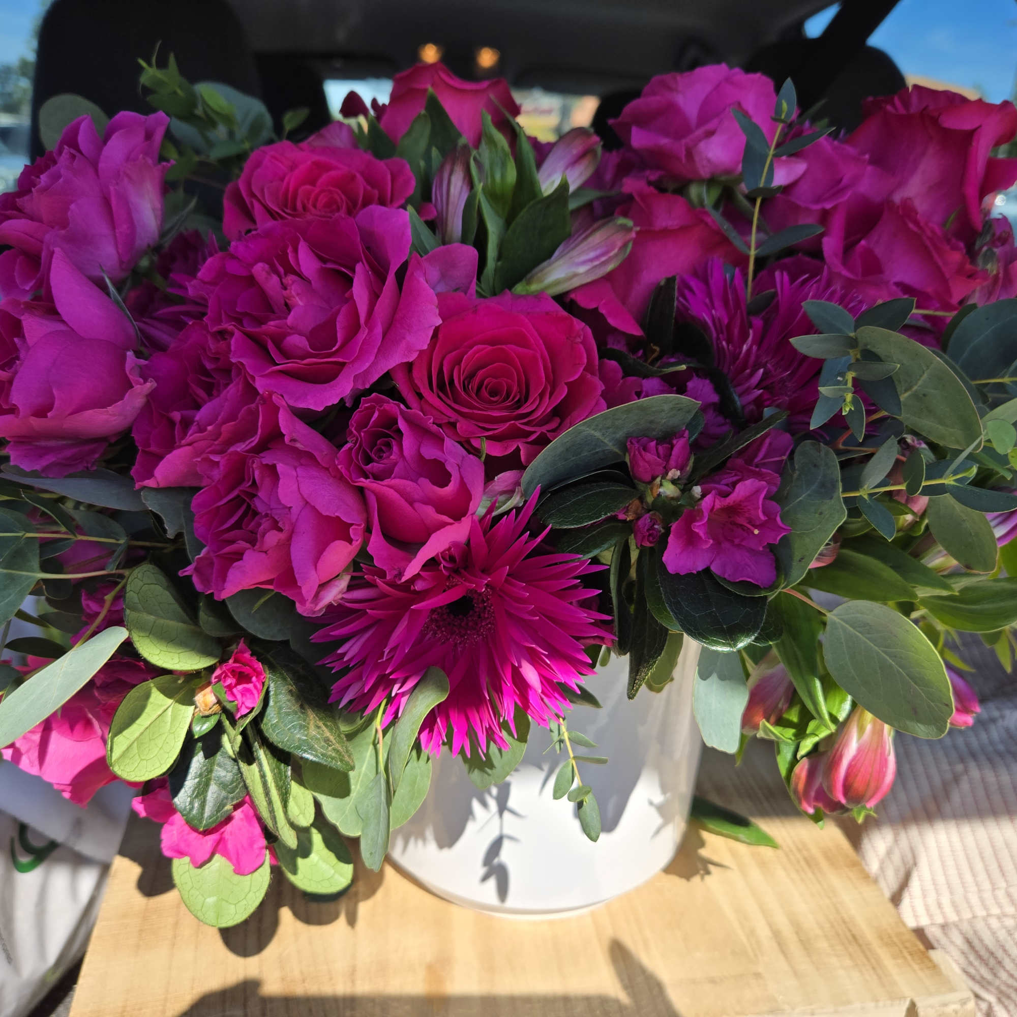 Bright pink rose bouquet in a white vase with mixed greenery