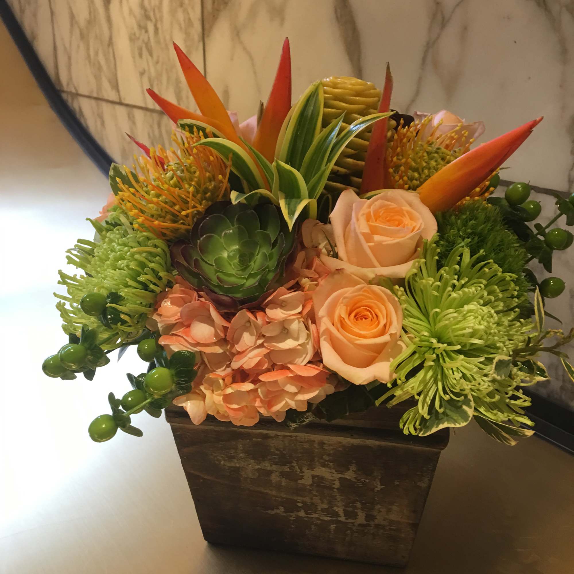 Tropical floral arrangement in a square wooden vase with peach roses and green succulents