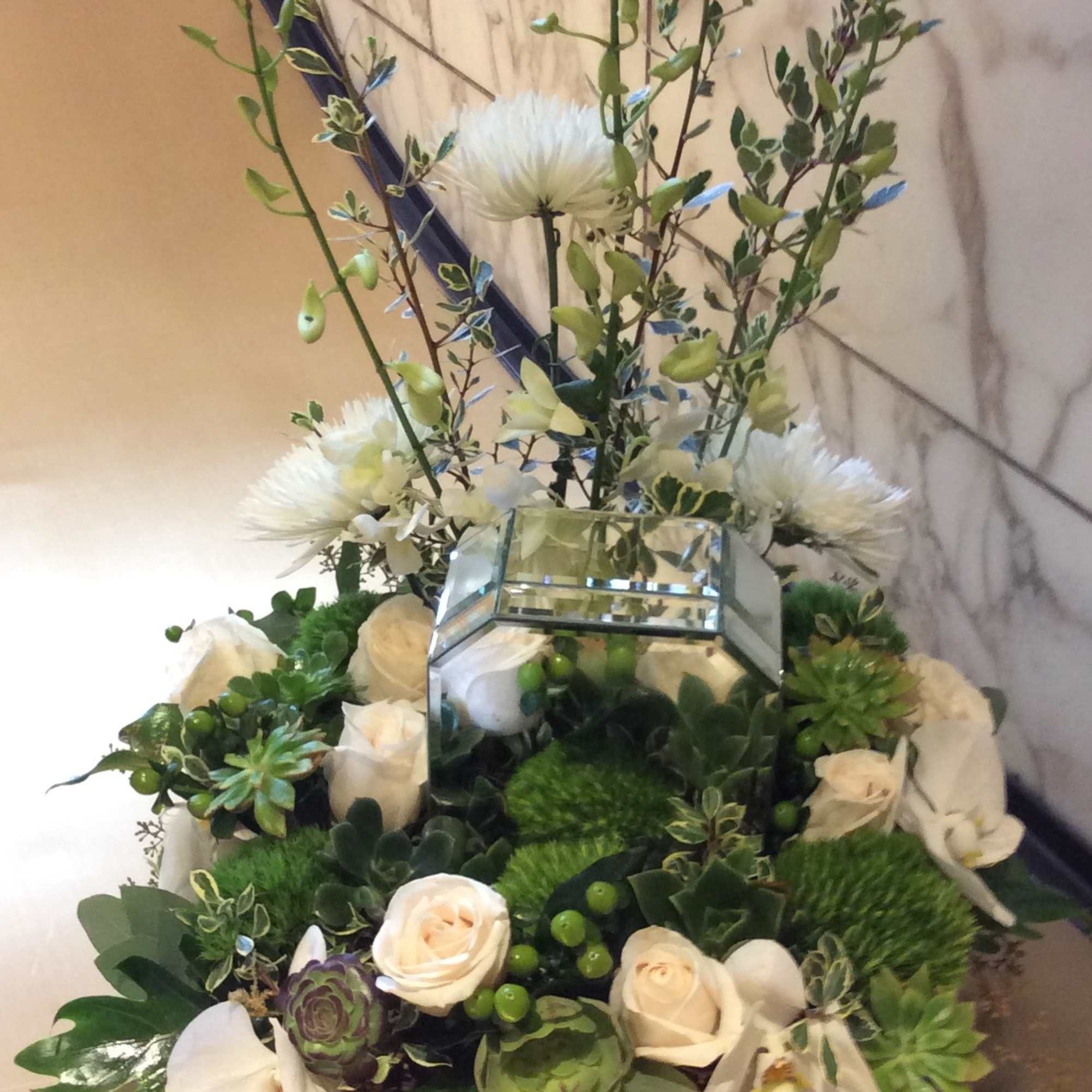White roses and orchids arranged with succulents in a mirrored vase