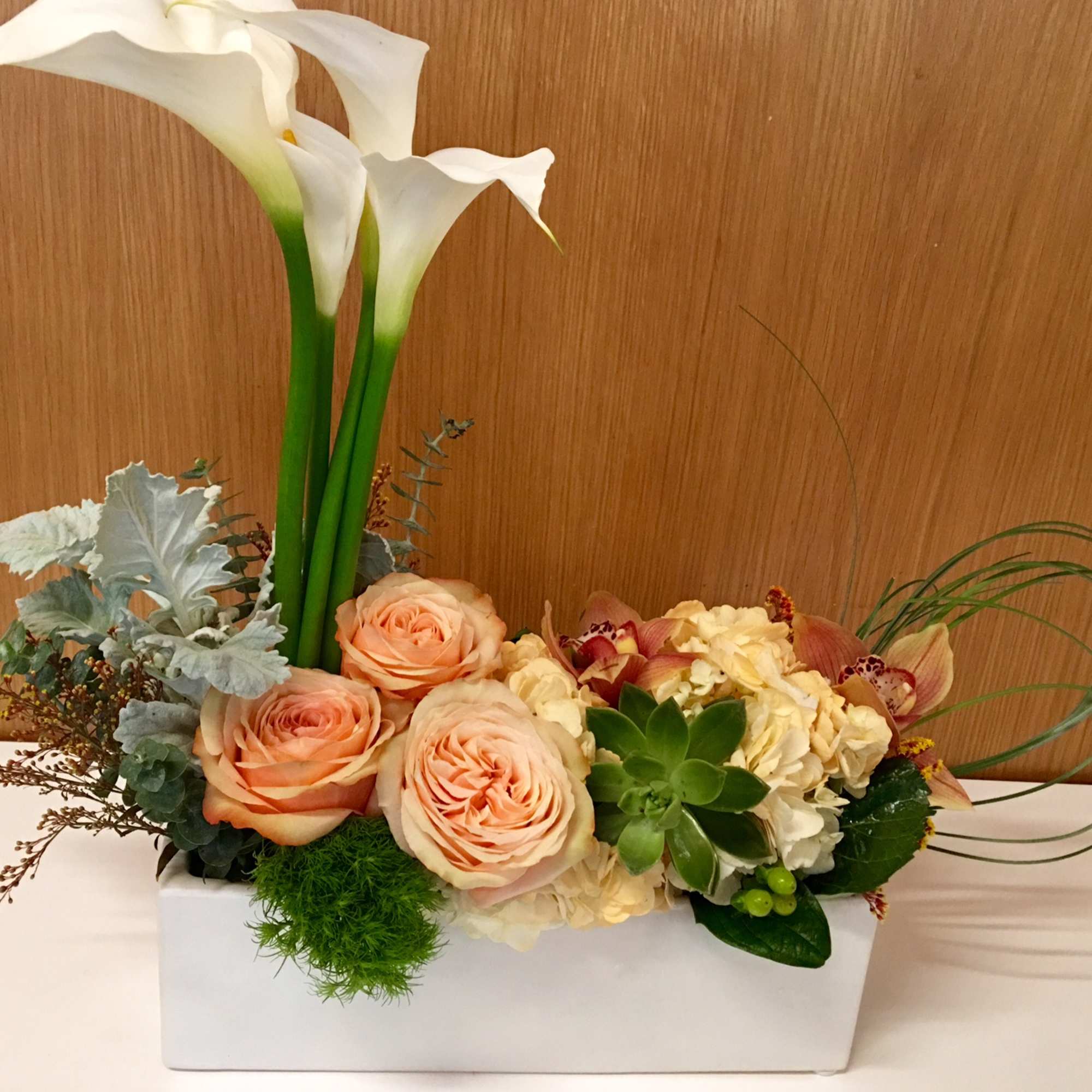 Peach roses and white calla lilies in a white rectangular vase