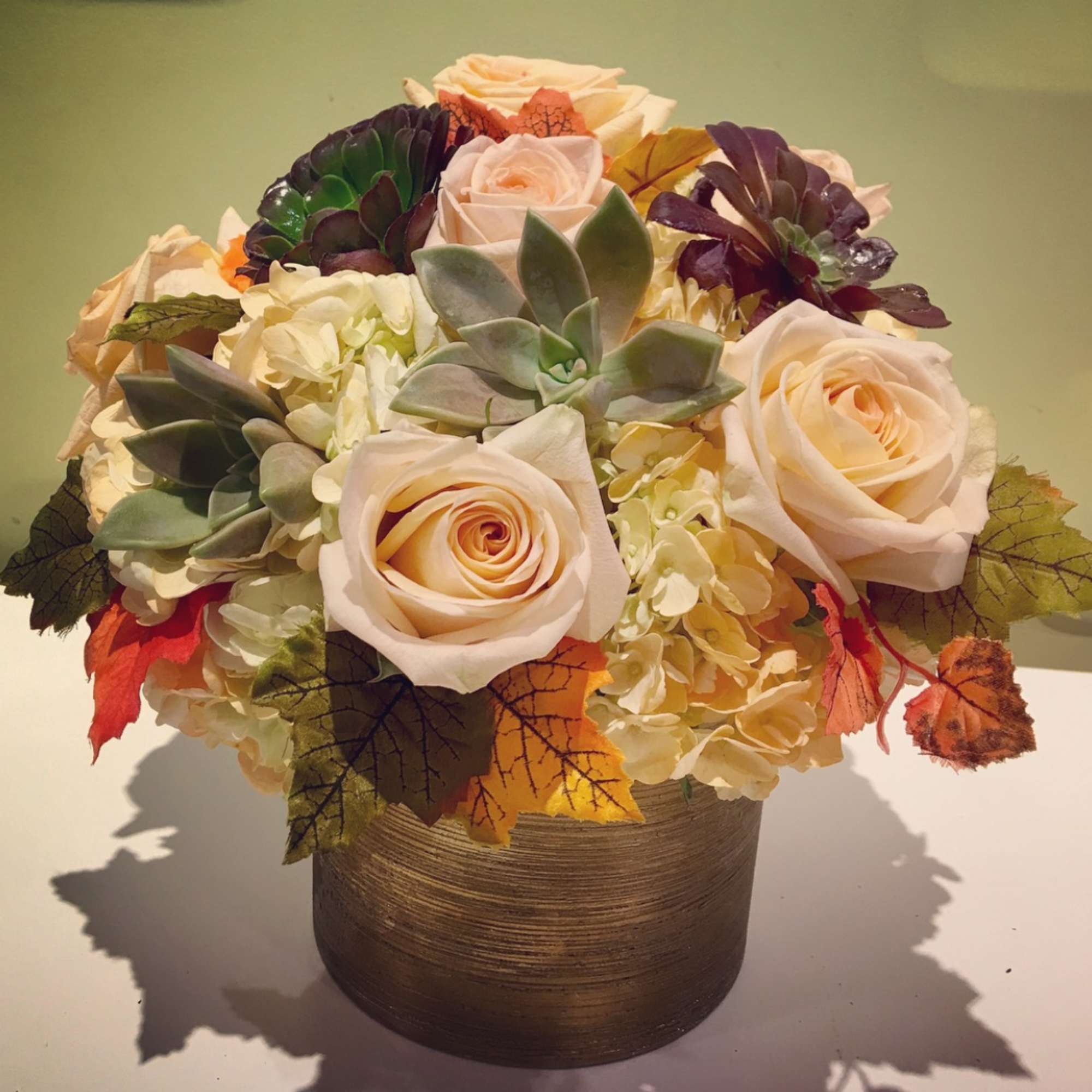 Bouquet of cream roses, succulents, and autumn leaves in a round vase