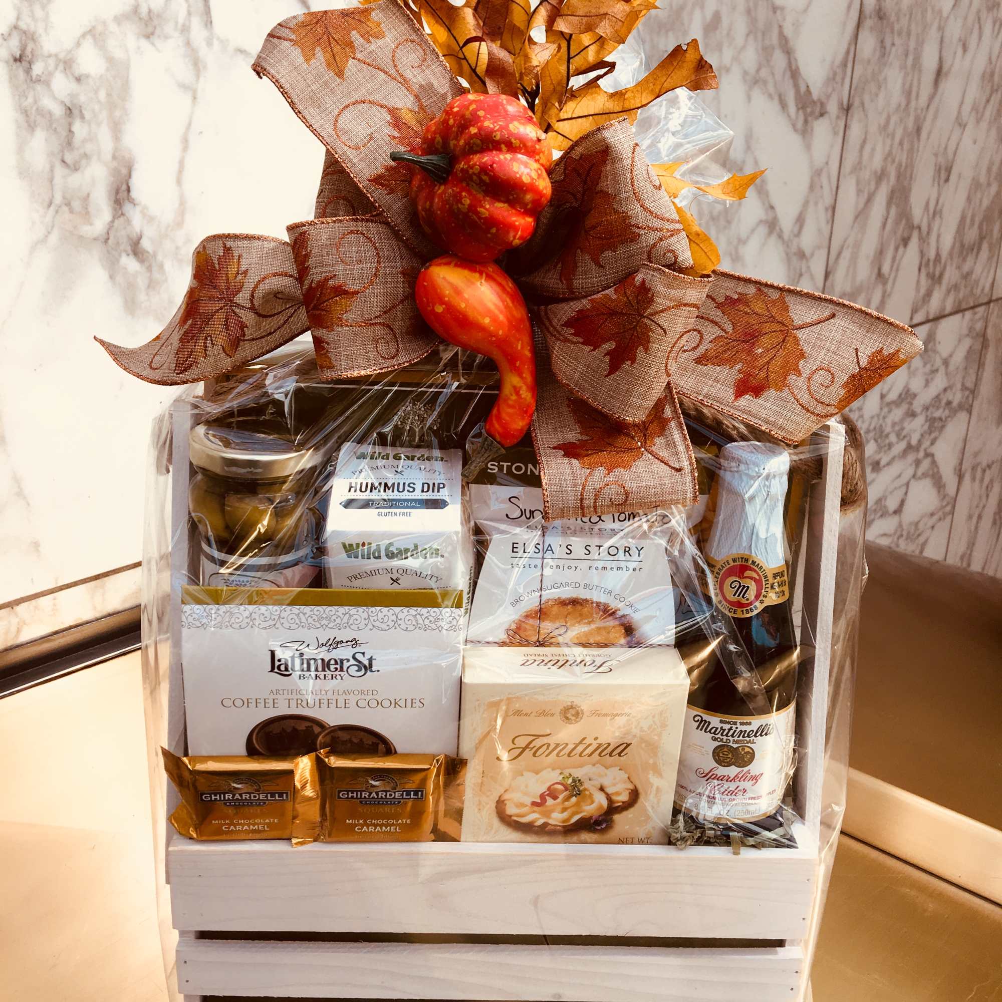 Gift basket with snacks, cookies, and a sparkling cider bottle topped with an autumn bow