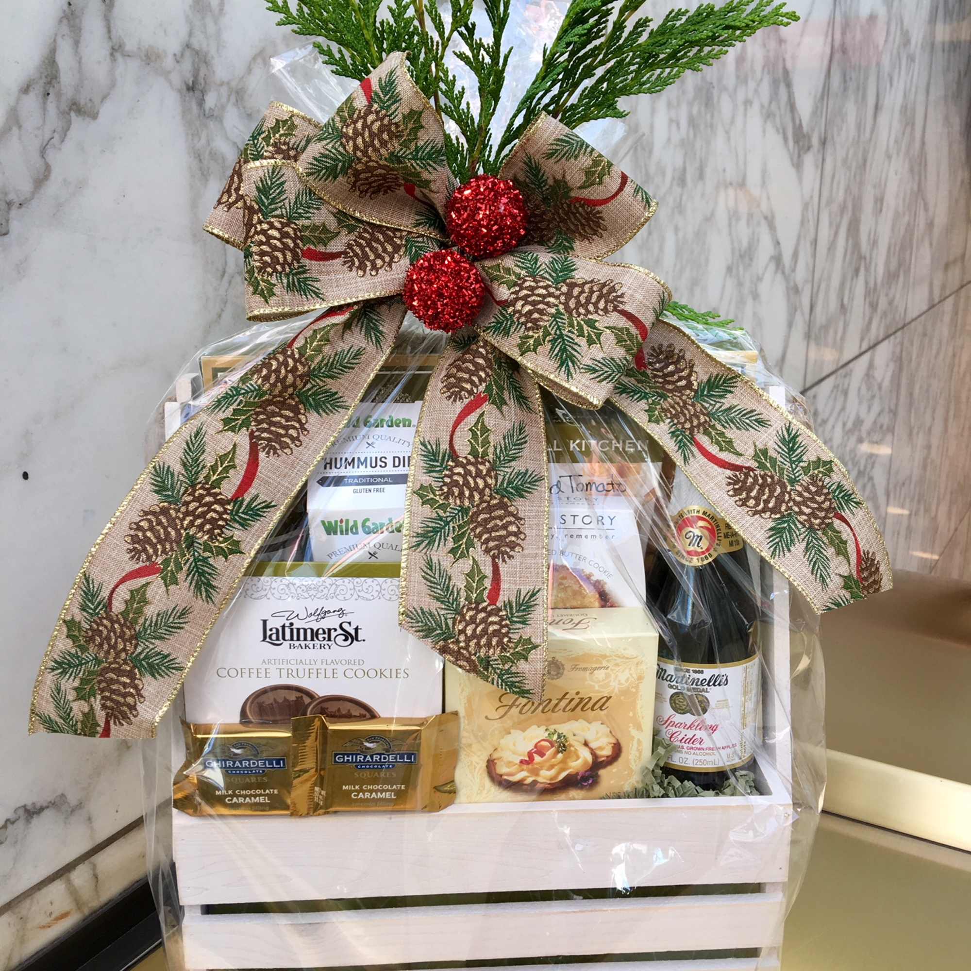 Holiday gift basket with snacks, cider, and a pinecone ribbon bow