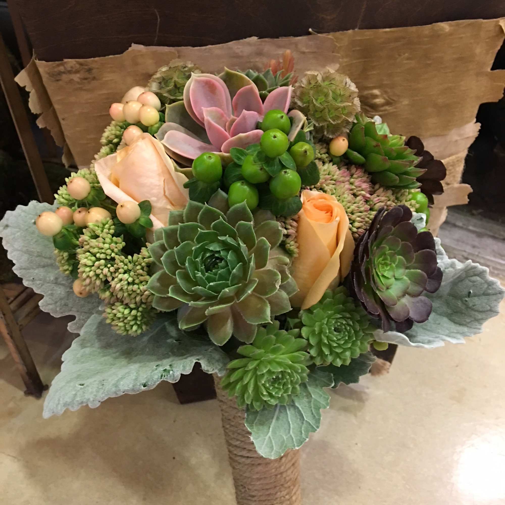 Succulent bouquet with peach roses and green berries wrapped in paper