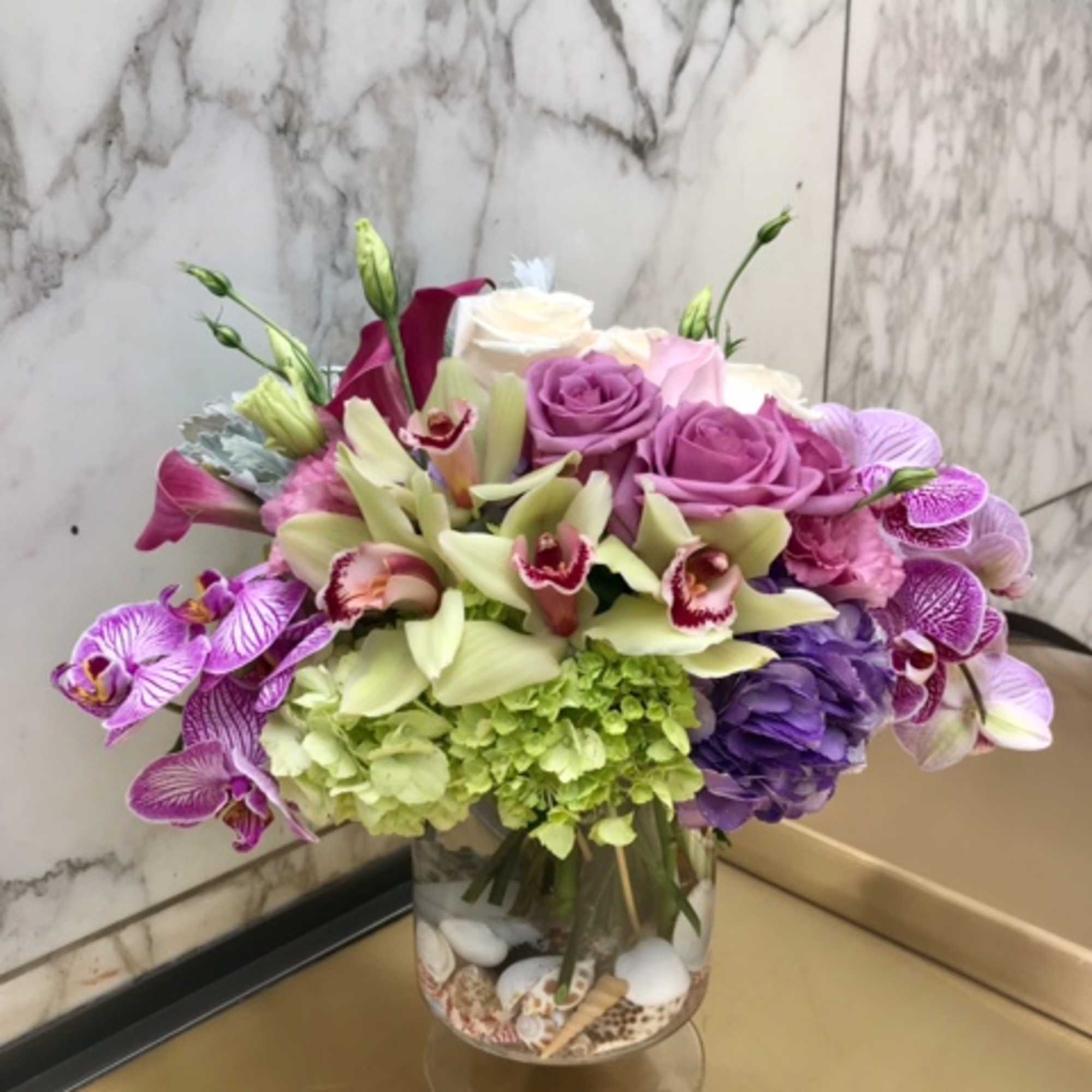 Mixed bouquet of roses, orchids, and hydrangeas in a glass vase