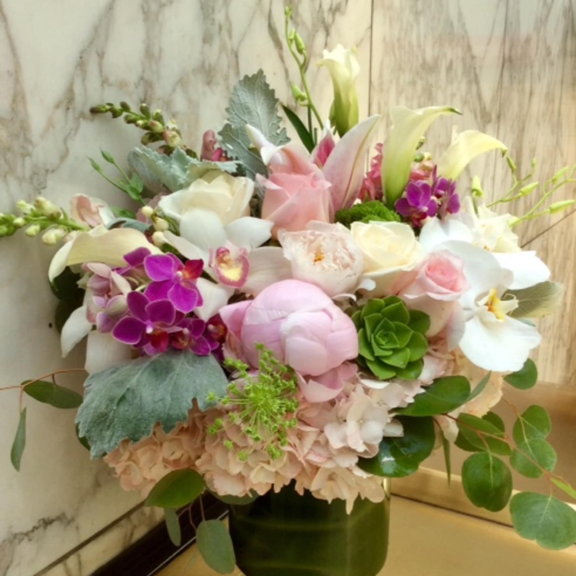 Mixed pastel bouquet in a glass vase with orchids, roses, and lilies