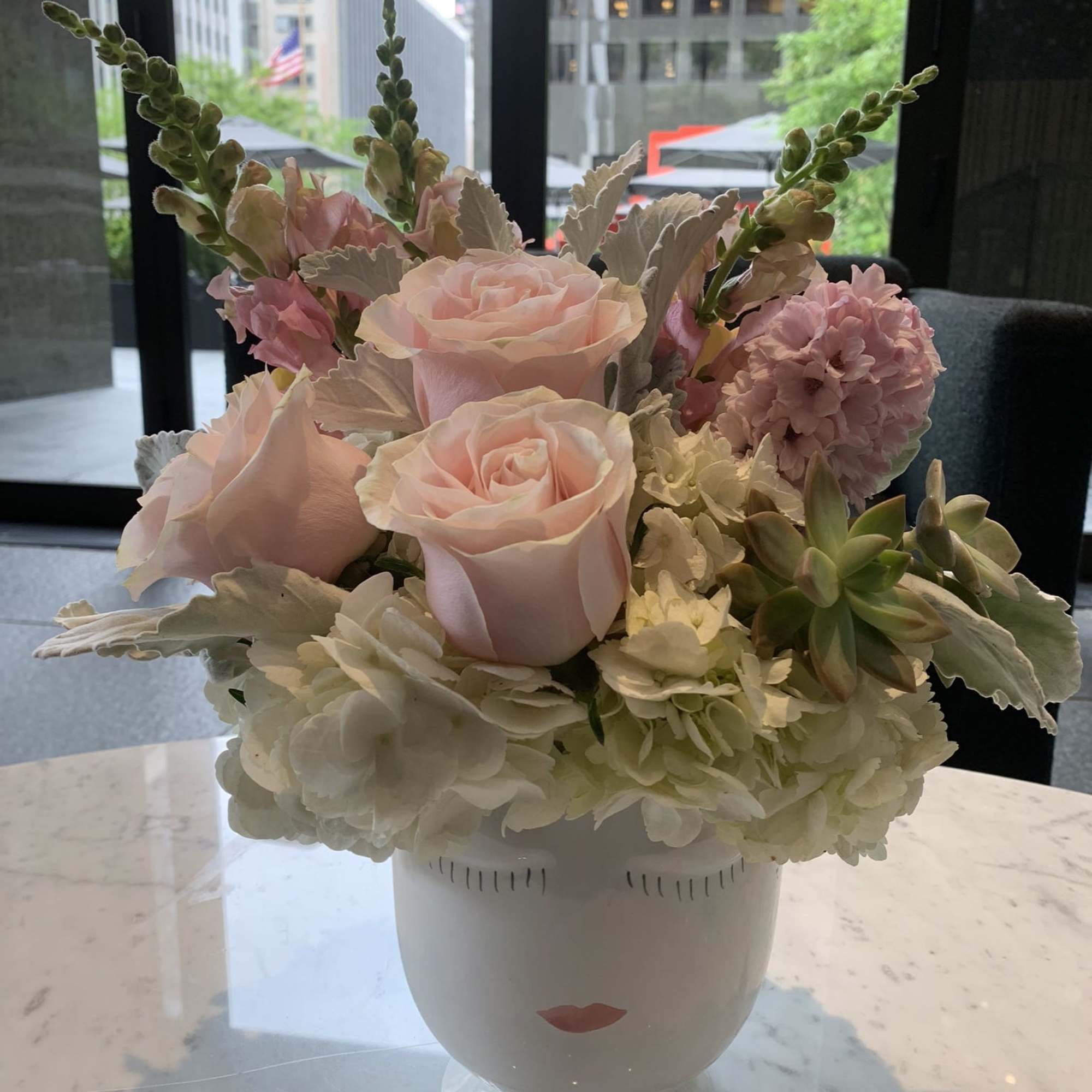 Pink roses and pale hydrangeas in a white vase with a face design