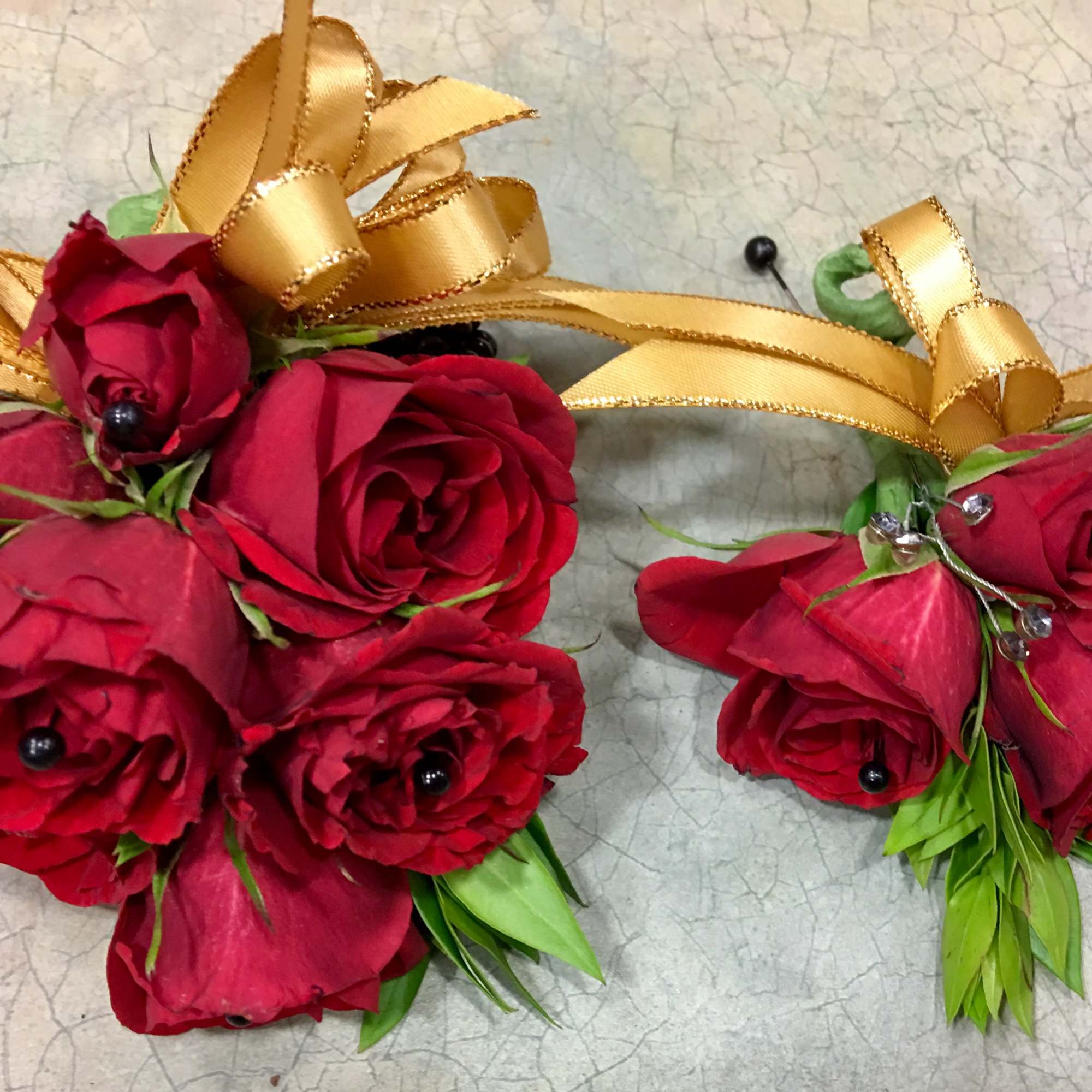 Two red rose corsages with gold ribbon bows