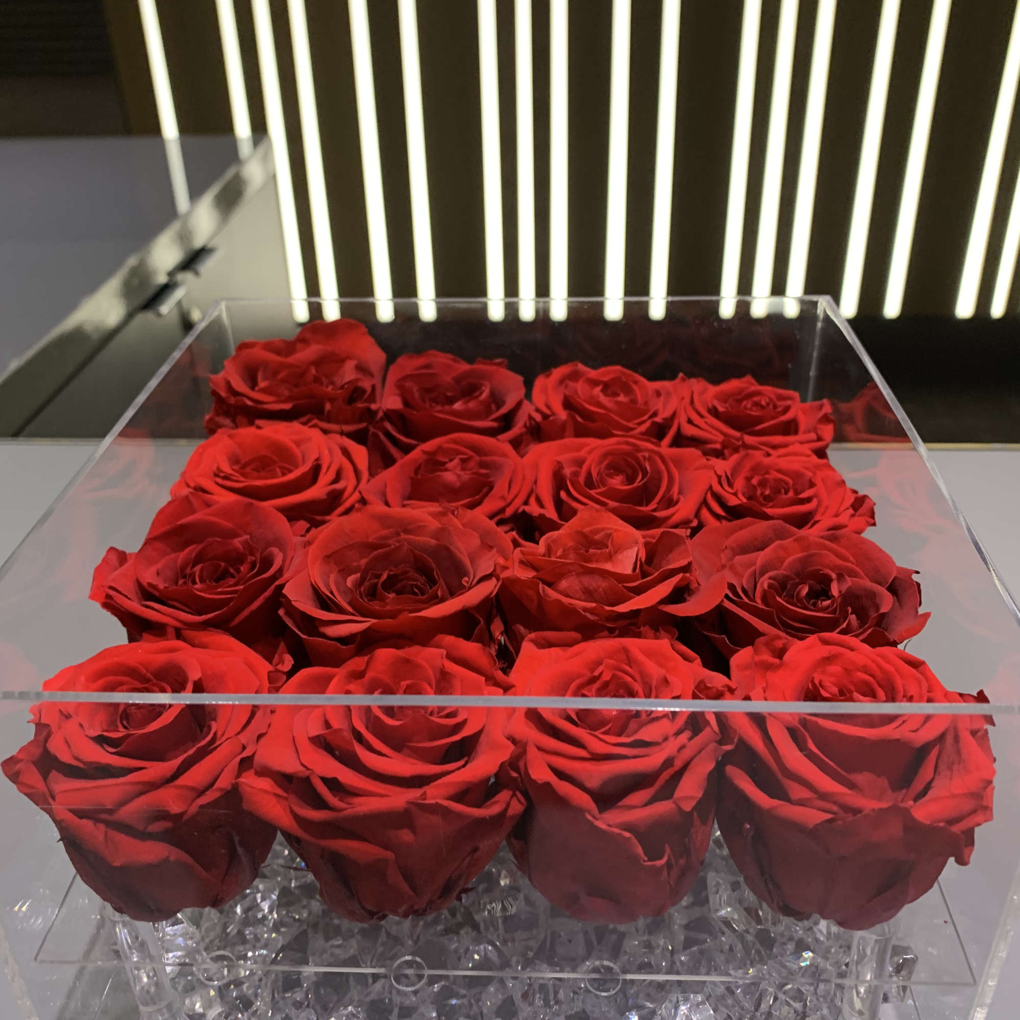 Red roses arranged in a clear acrylic box with crystal filler