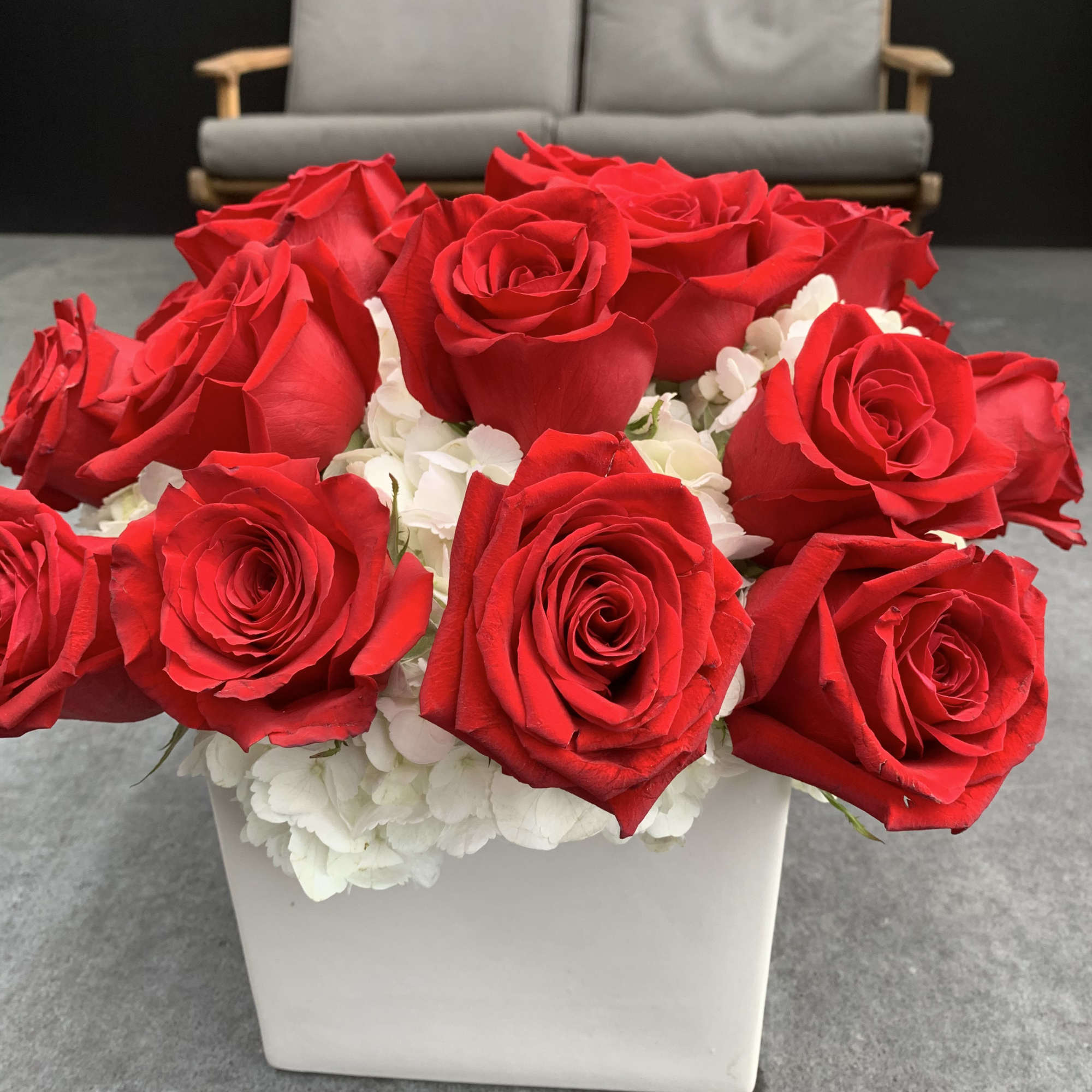 Red roses arranged in a white square vase with white hydrangeas