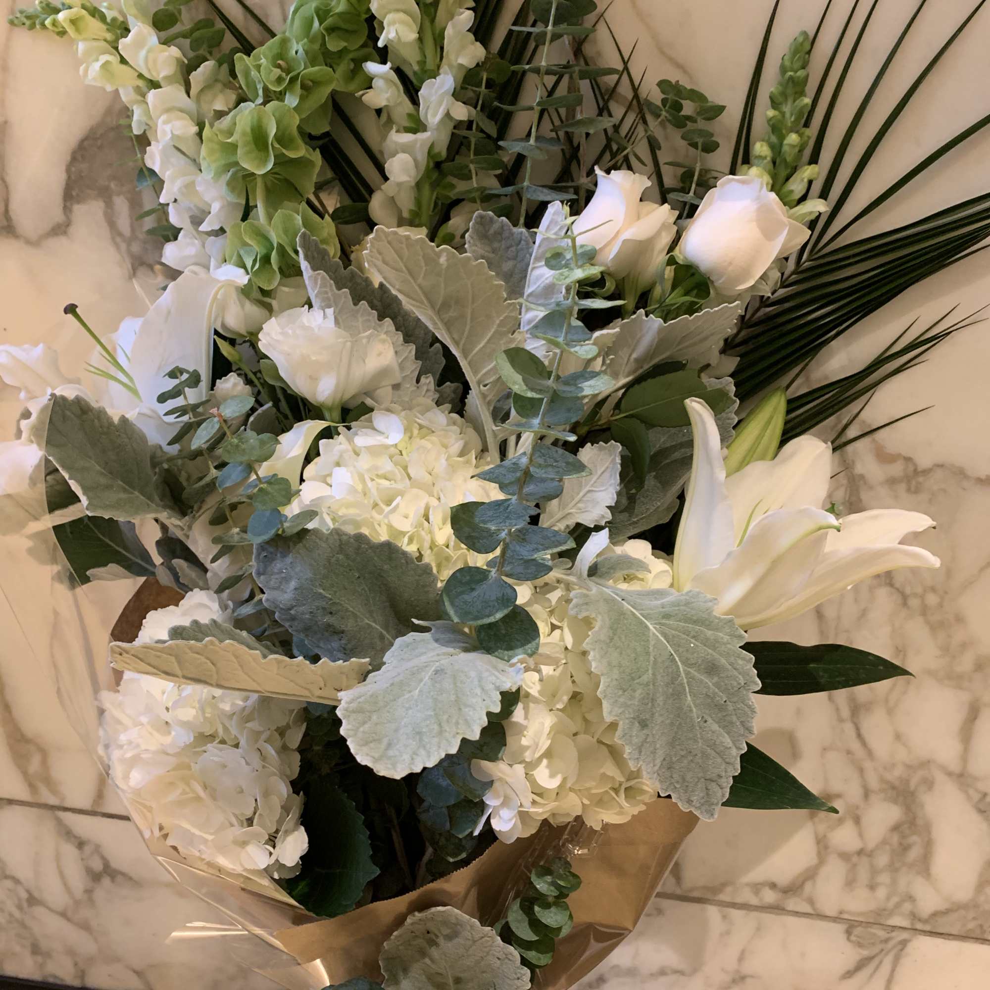 White floral bouquet with lilies and hydrangeas wrapped in brown paper