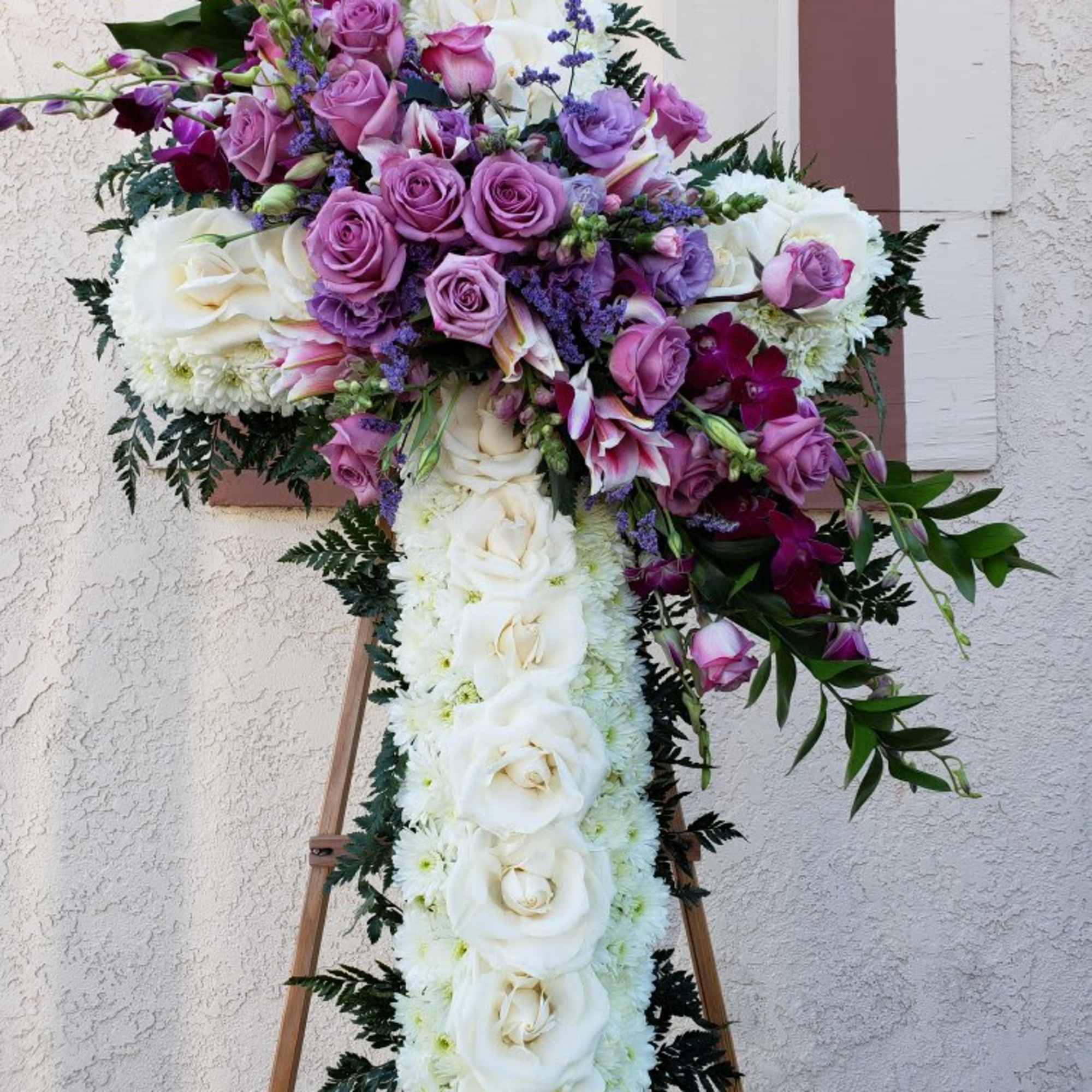 Large cross-shaped floral tribute with white and purple flowers on an easel