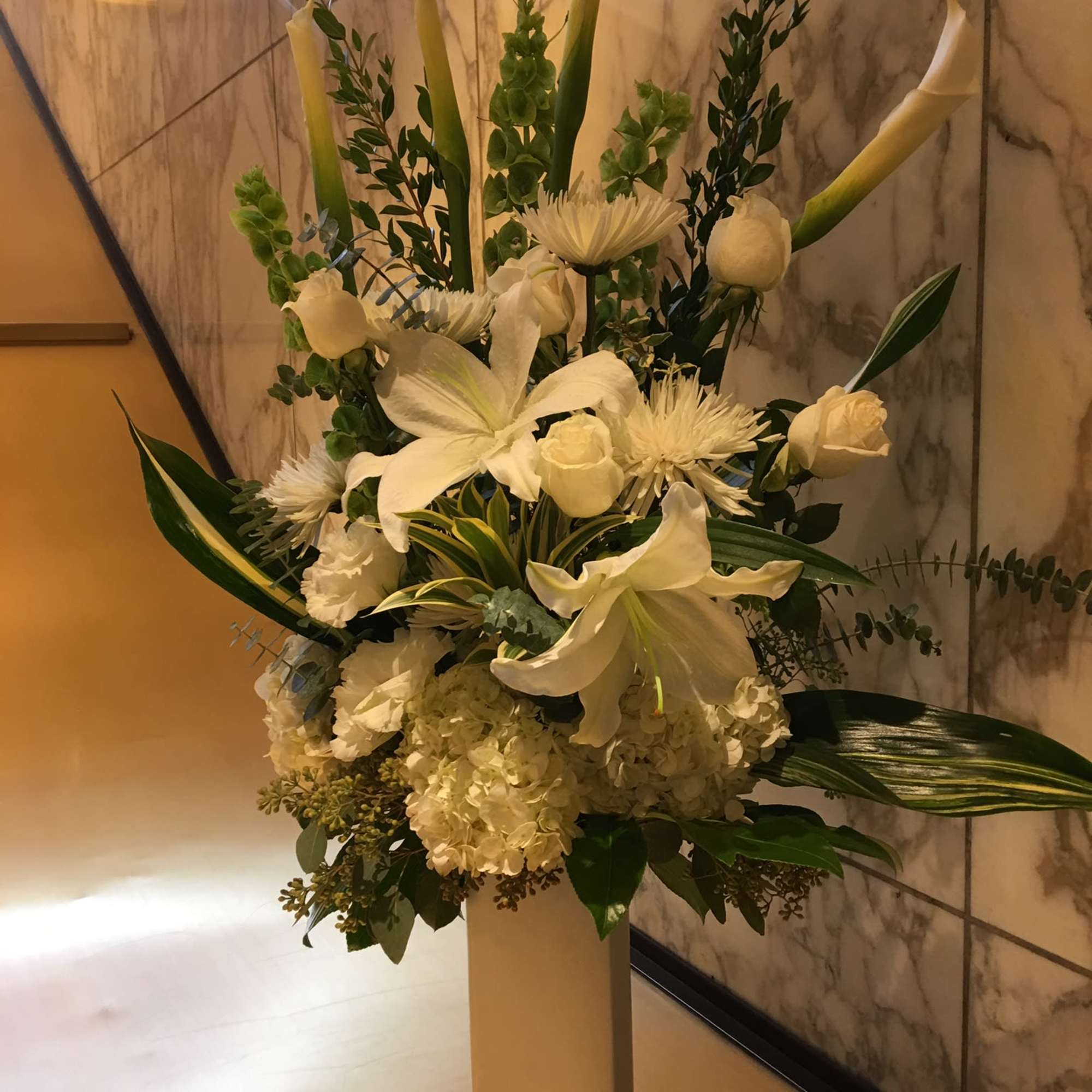 Tall white floral arrangement in a square pedestal vase