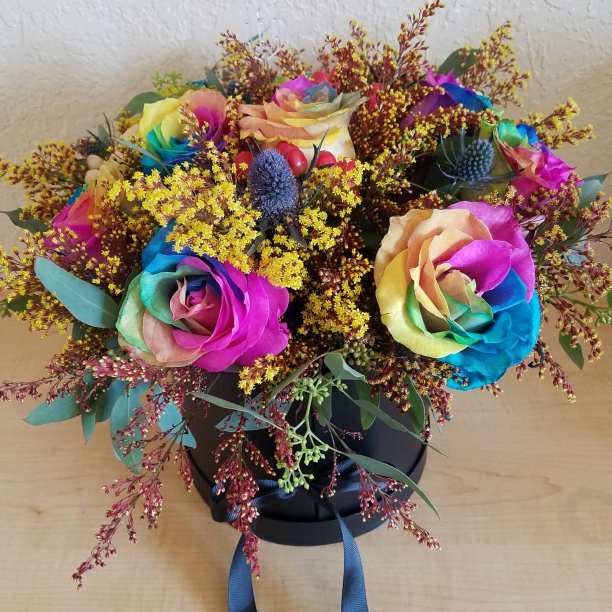 Rainbow-colored roses in a black hatbox with blue ribbon