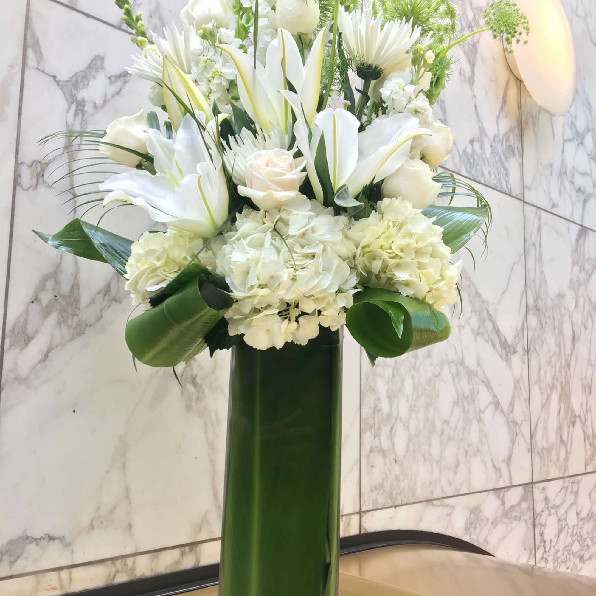 Tall white floral arrangement in a green glass vase