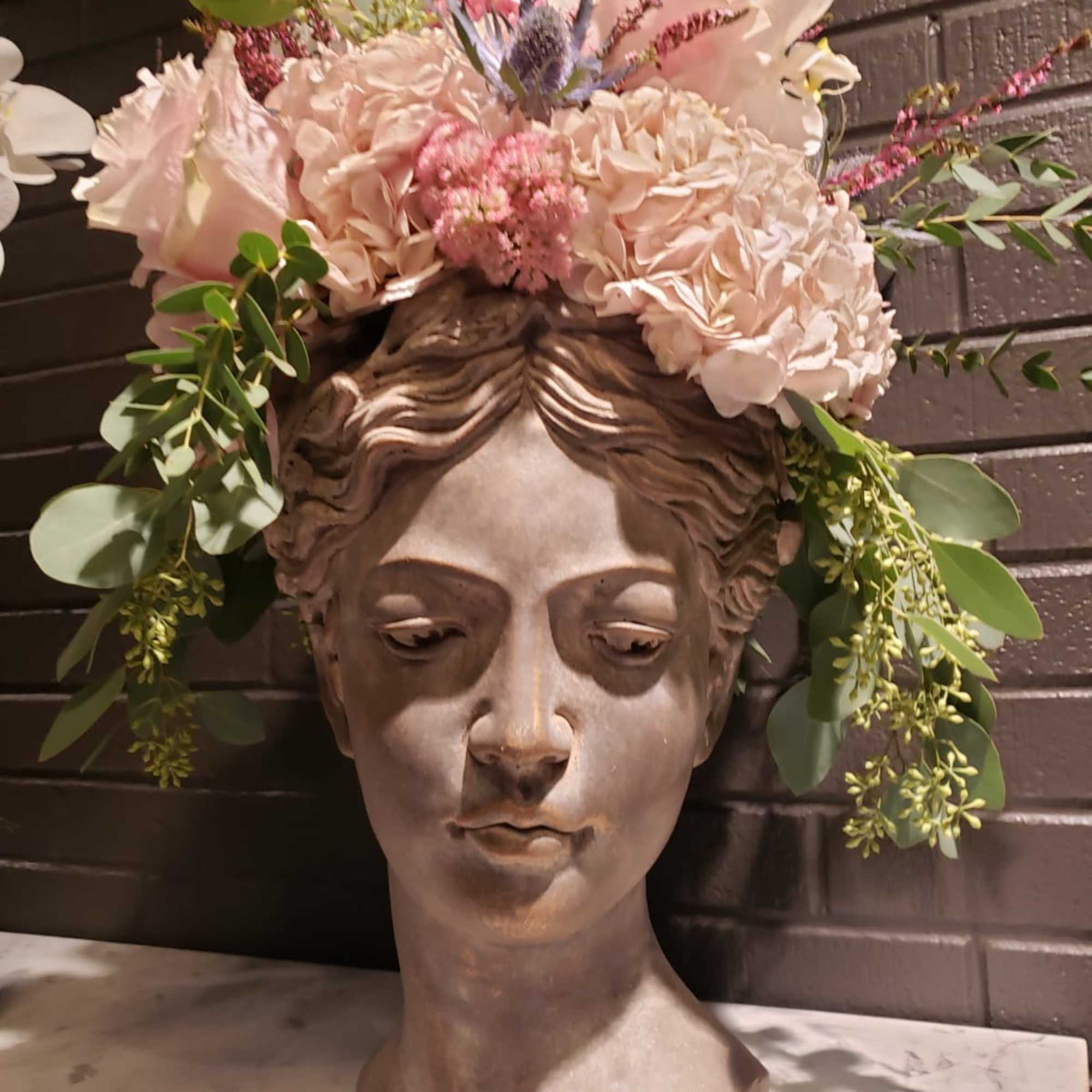 Floral crown on a sculpted female bust with pale pink and white flowers