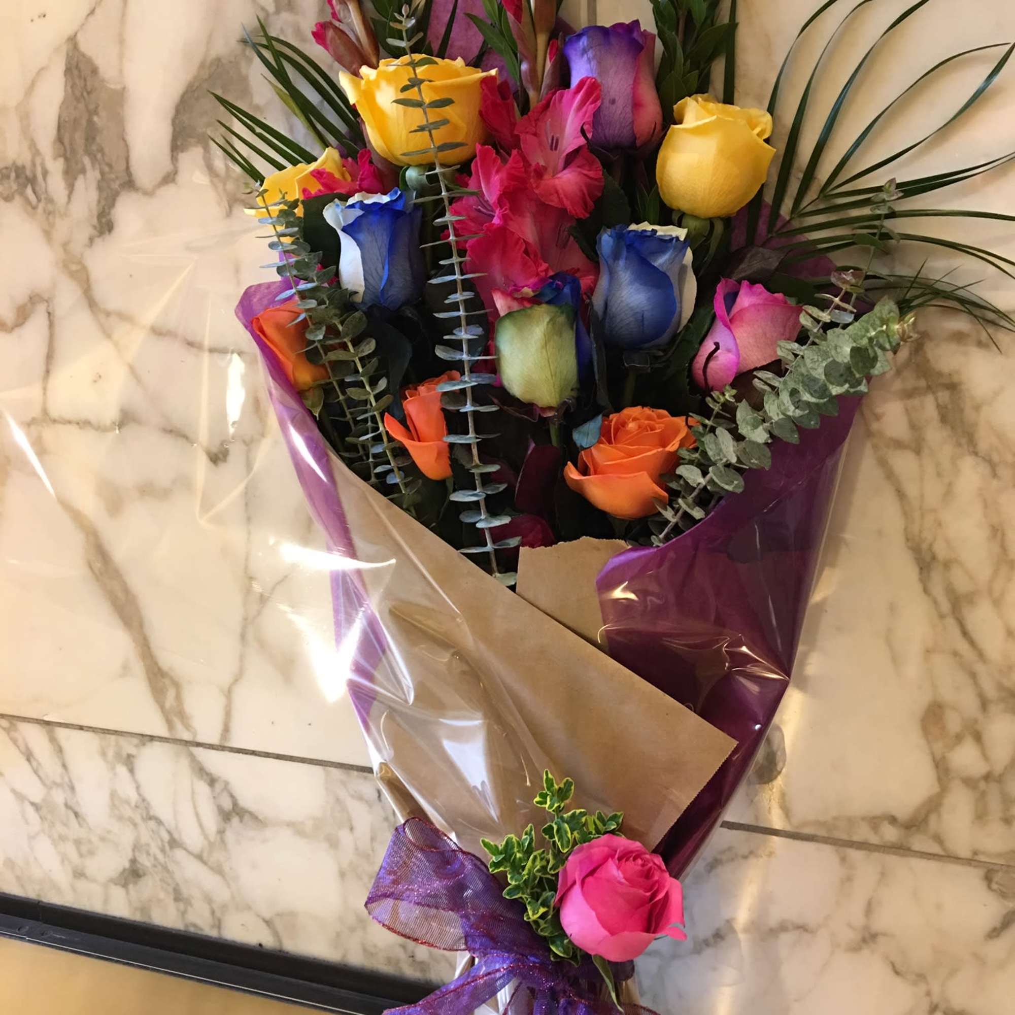Bouquet of multicolored roses wrapped in purple paper with a ribbon