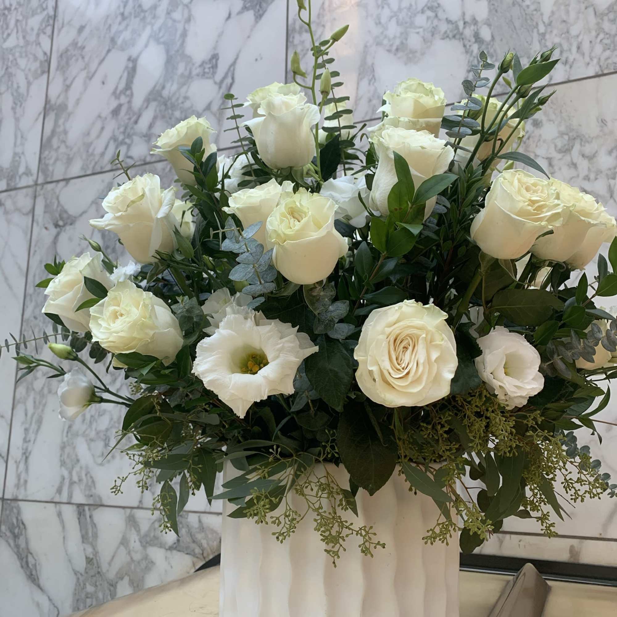 White roses and lisianthus in a white vase with greenery