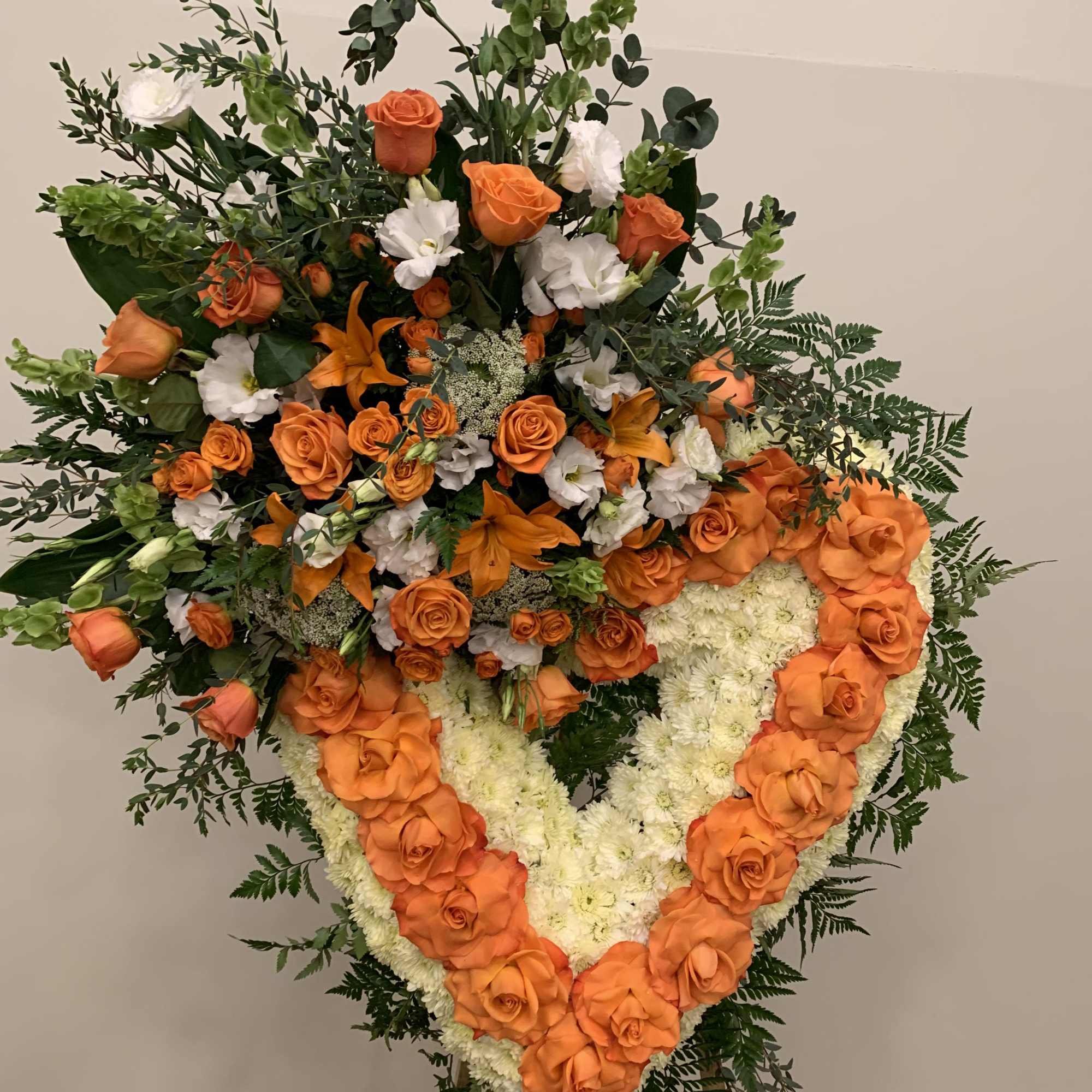 Large heart-shaped floral tribute with orange roses and white flowers