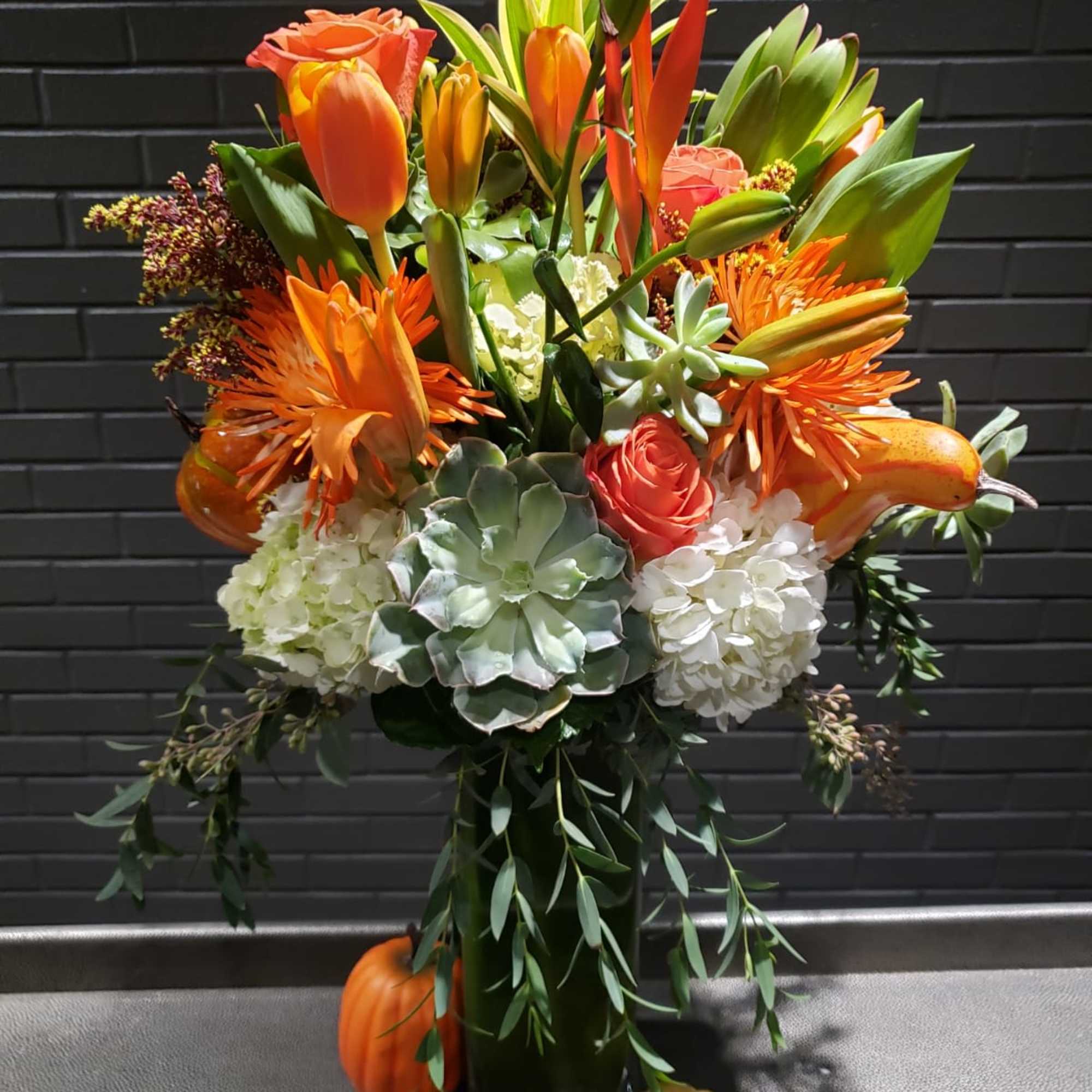Orange and white floral arrangement in a tall vase with pumpkins at the base