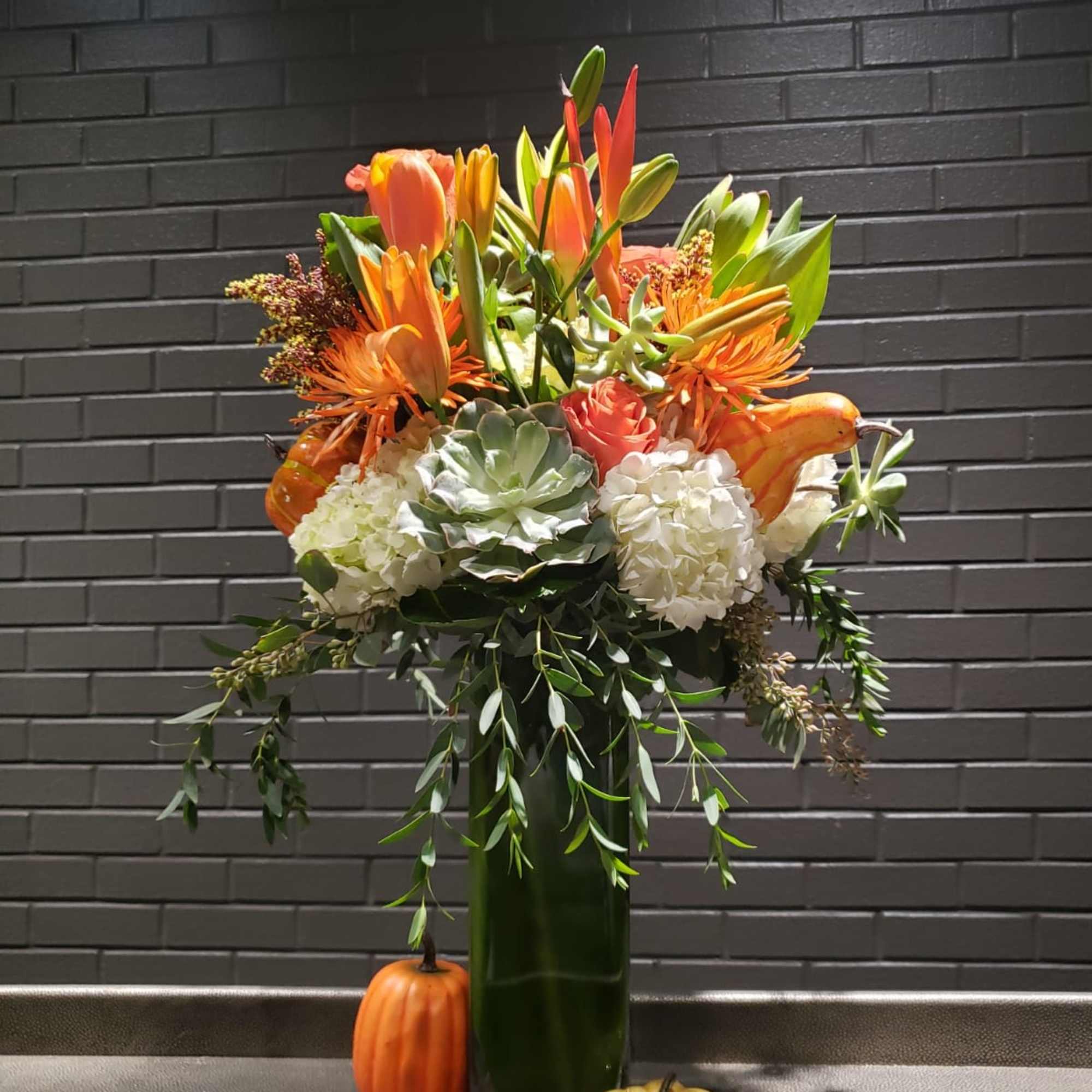 Orange and white floral arrangement in a tall green vase with pumpkins