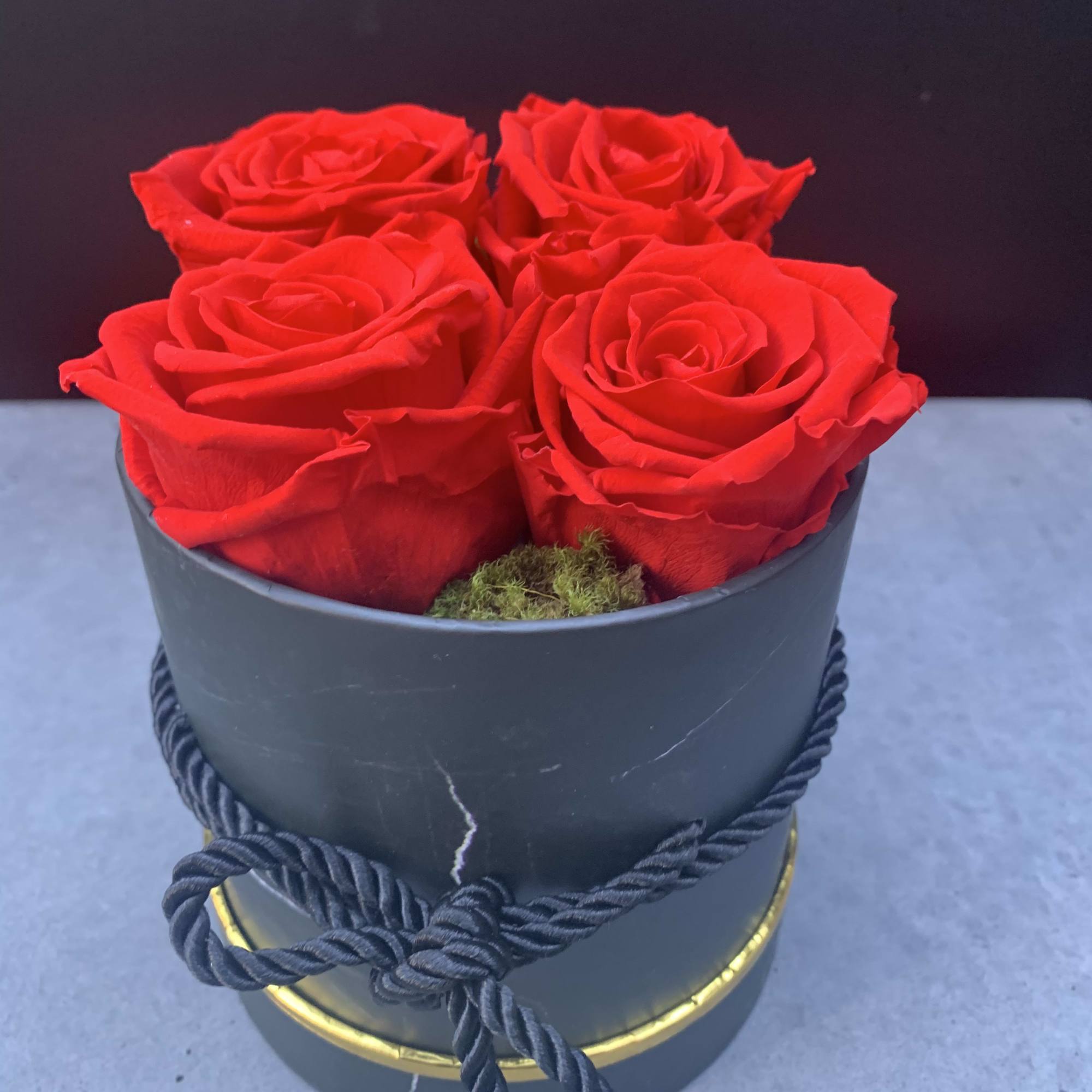 Four red roses in a black hatbox with a rope tie