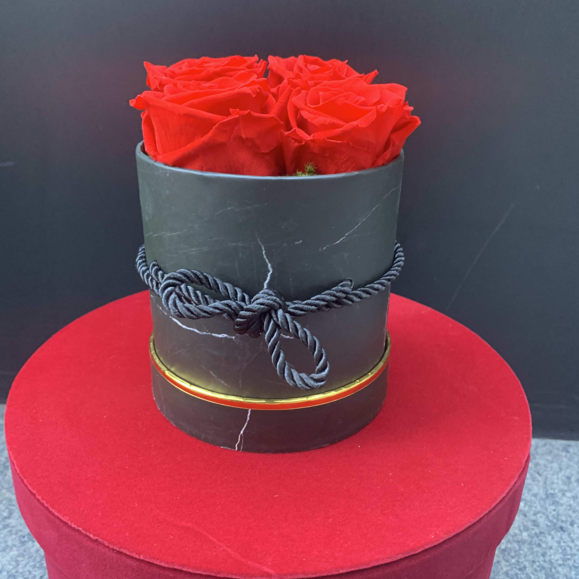 Red roses arranged in a black round box with a rope bow