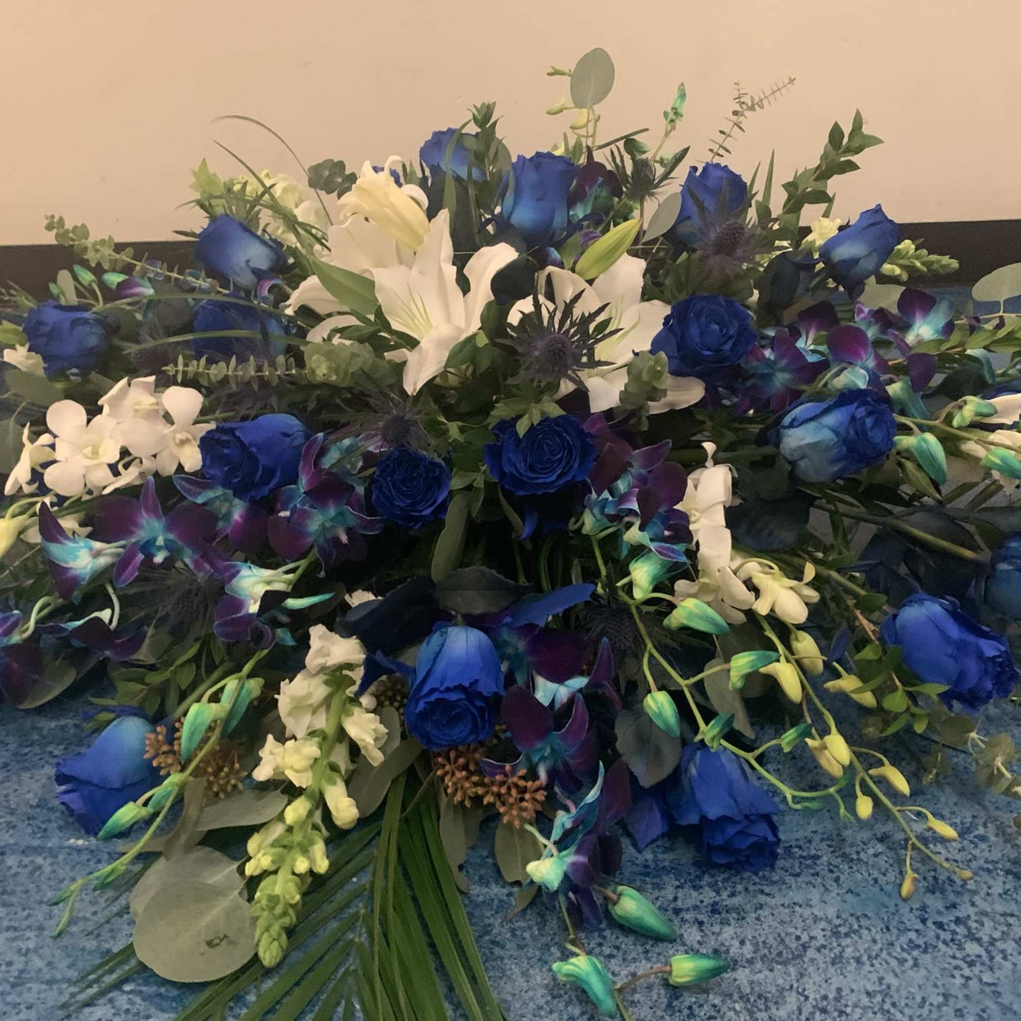 Blue roses and white lilies arranged with orchids and greenery