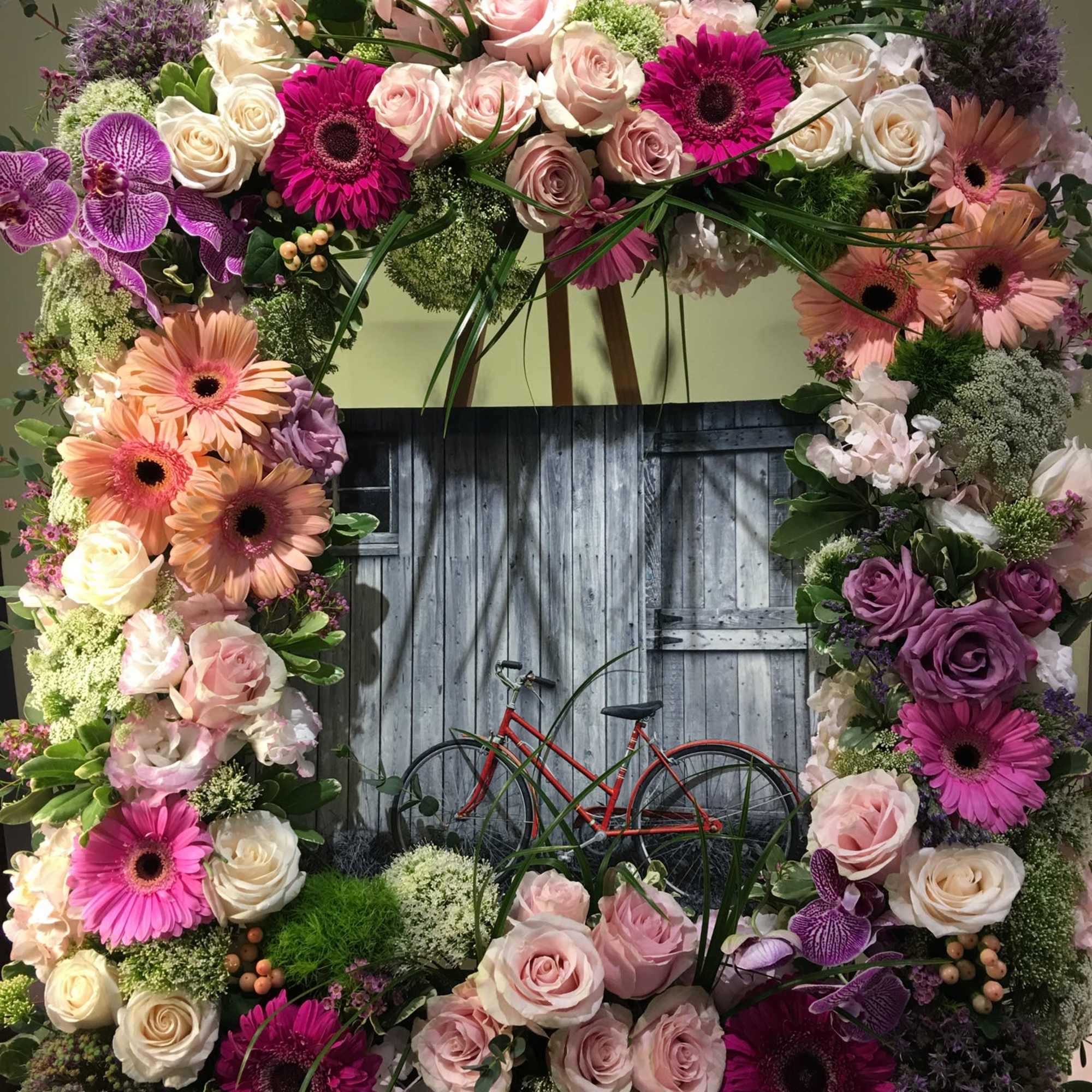 Large floral wreath with pink, purple, and cream blooms around a bicycle scene