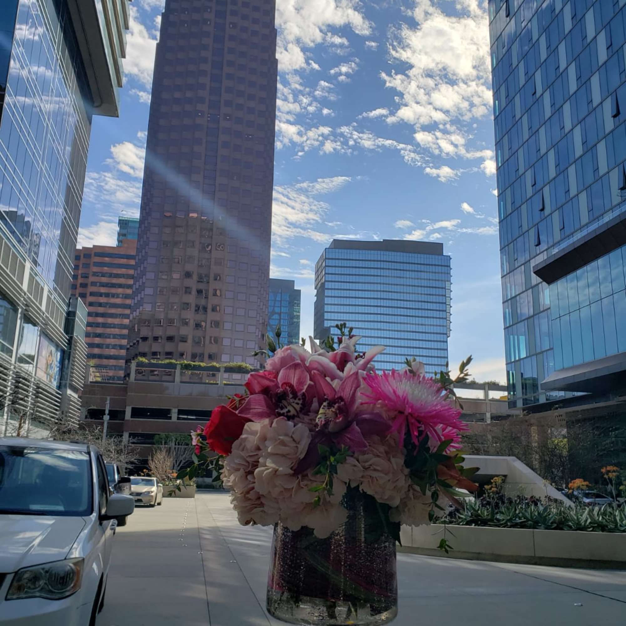 Large pink floral arrangement in a glass vase outdoors among city buildings