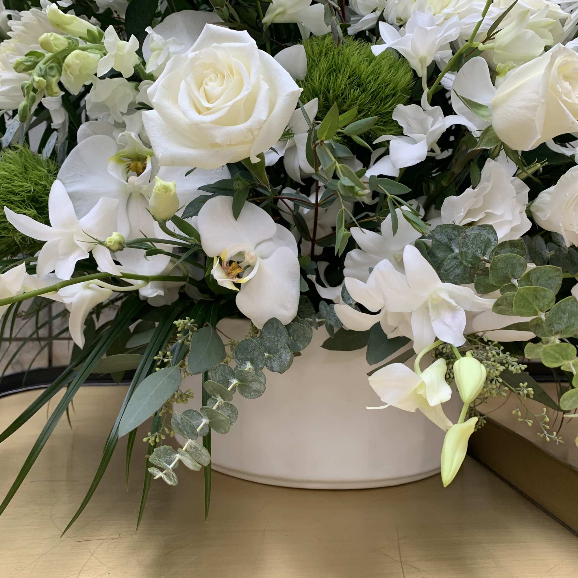 White roses and orchids arranged in a white container