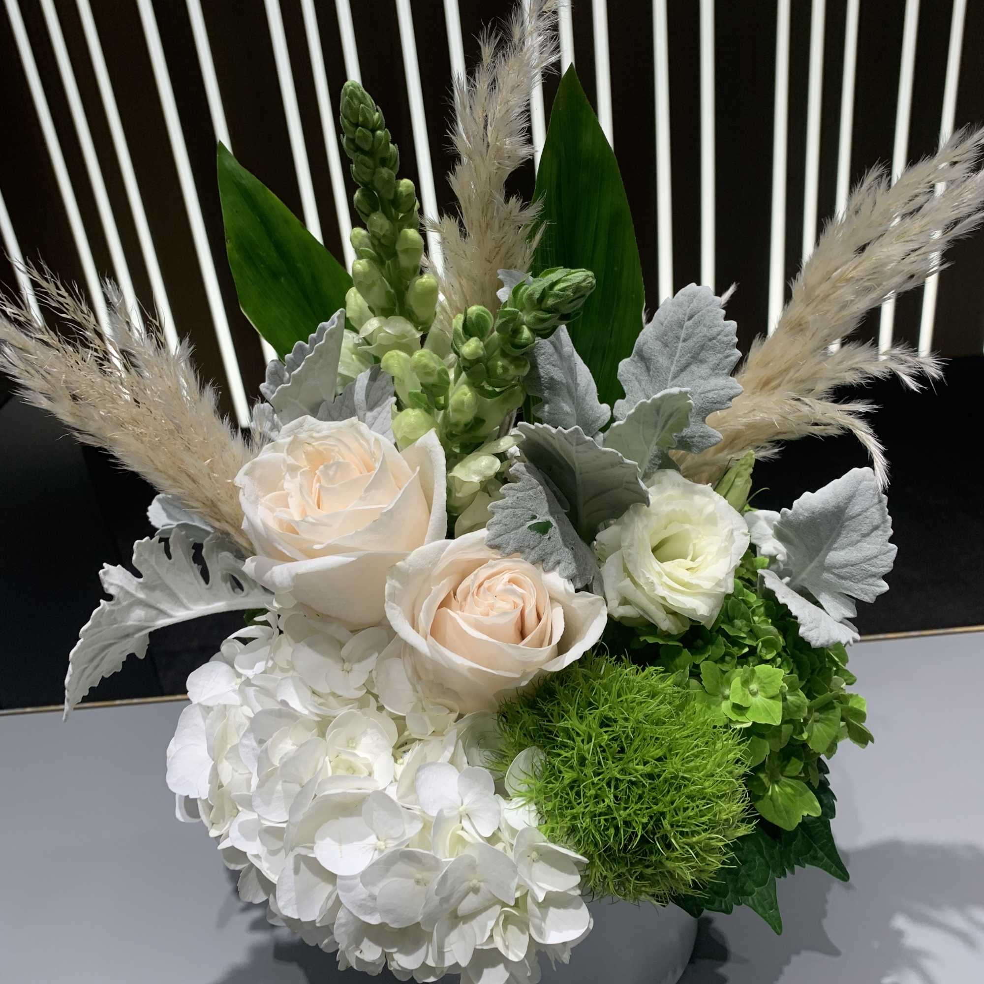 White and pale peach floral arrangement in a gray vase with green accents