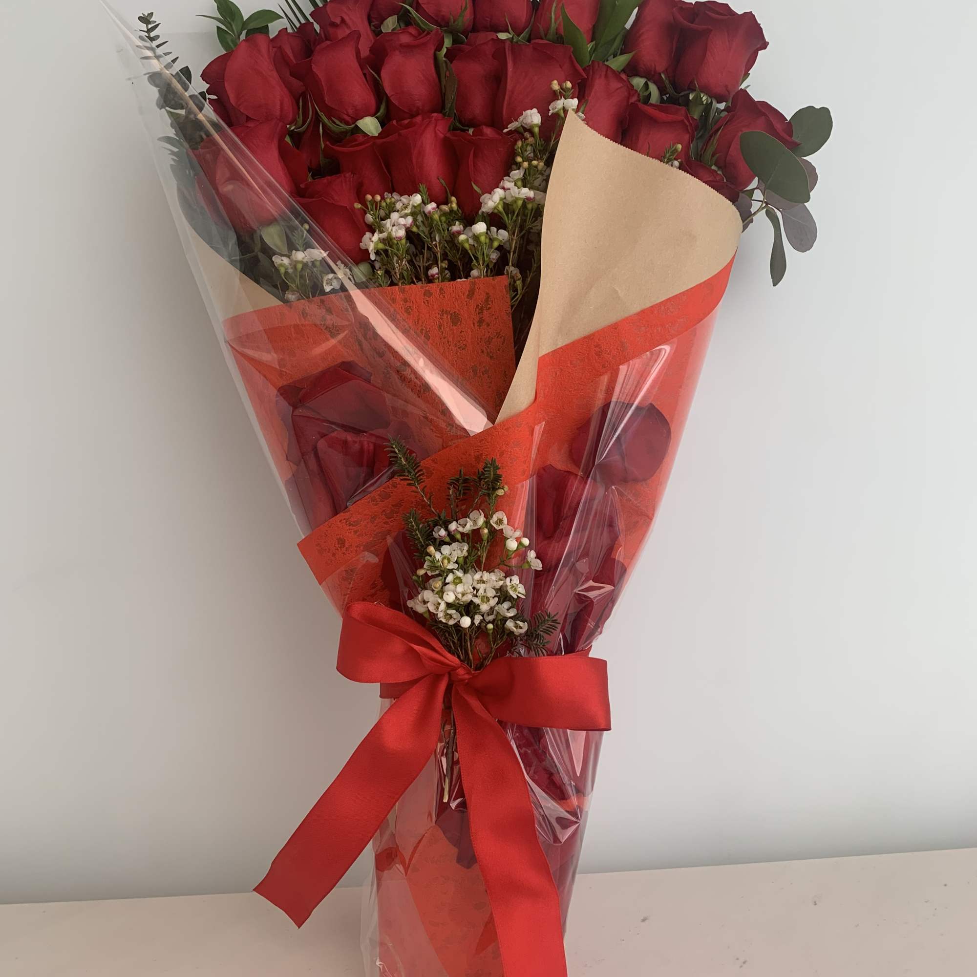 Bouquet of red roses wrapped in clear and red paper with a red ribbon