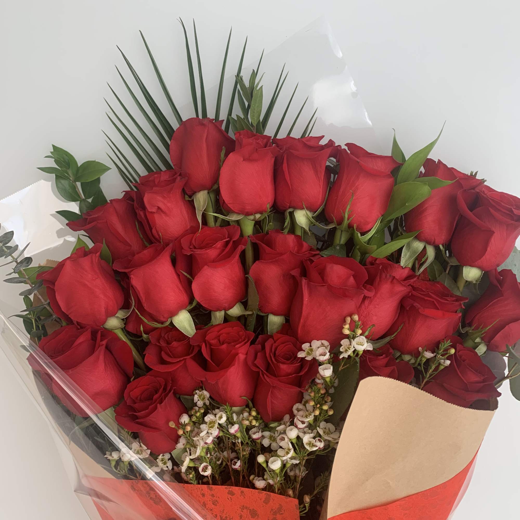Bouquet of red roses with small white filler flowers and palm fronds
