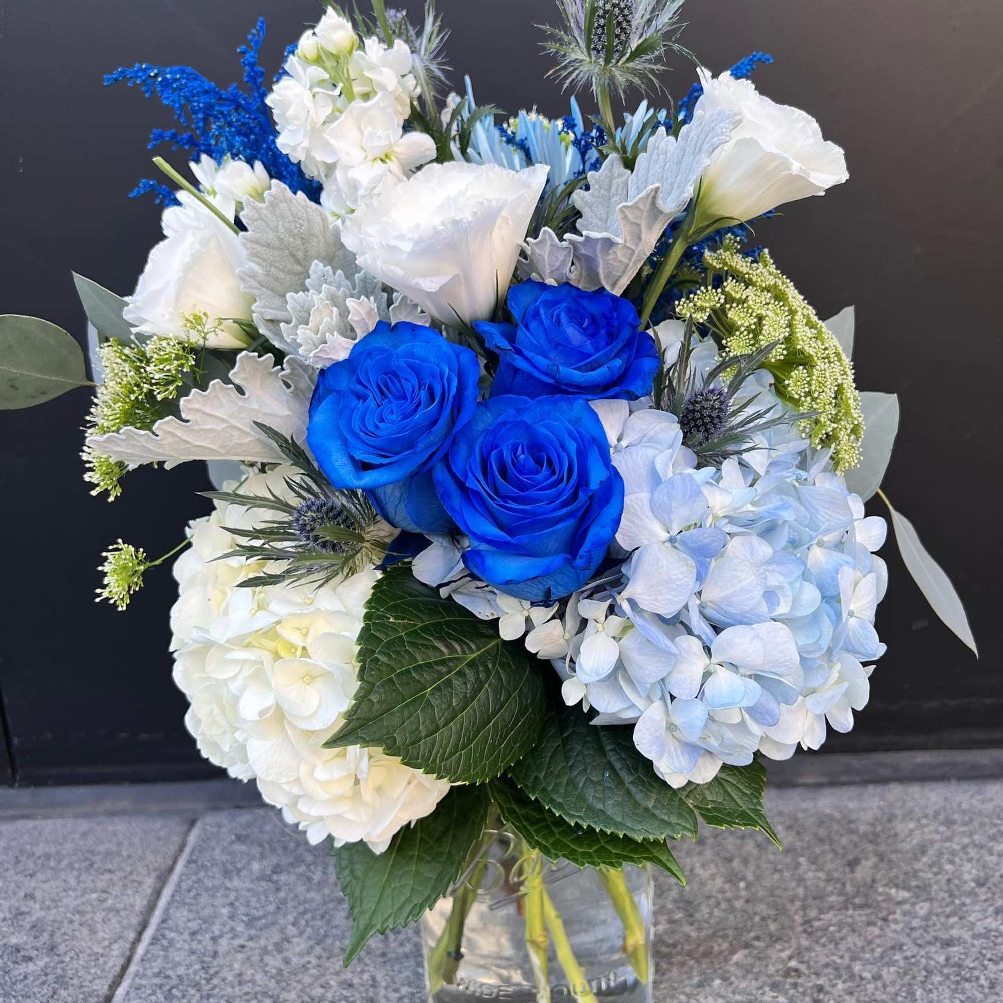 Blue roses and white hydrangeas in a clear glass vase