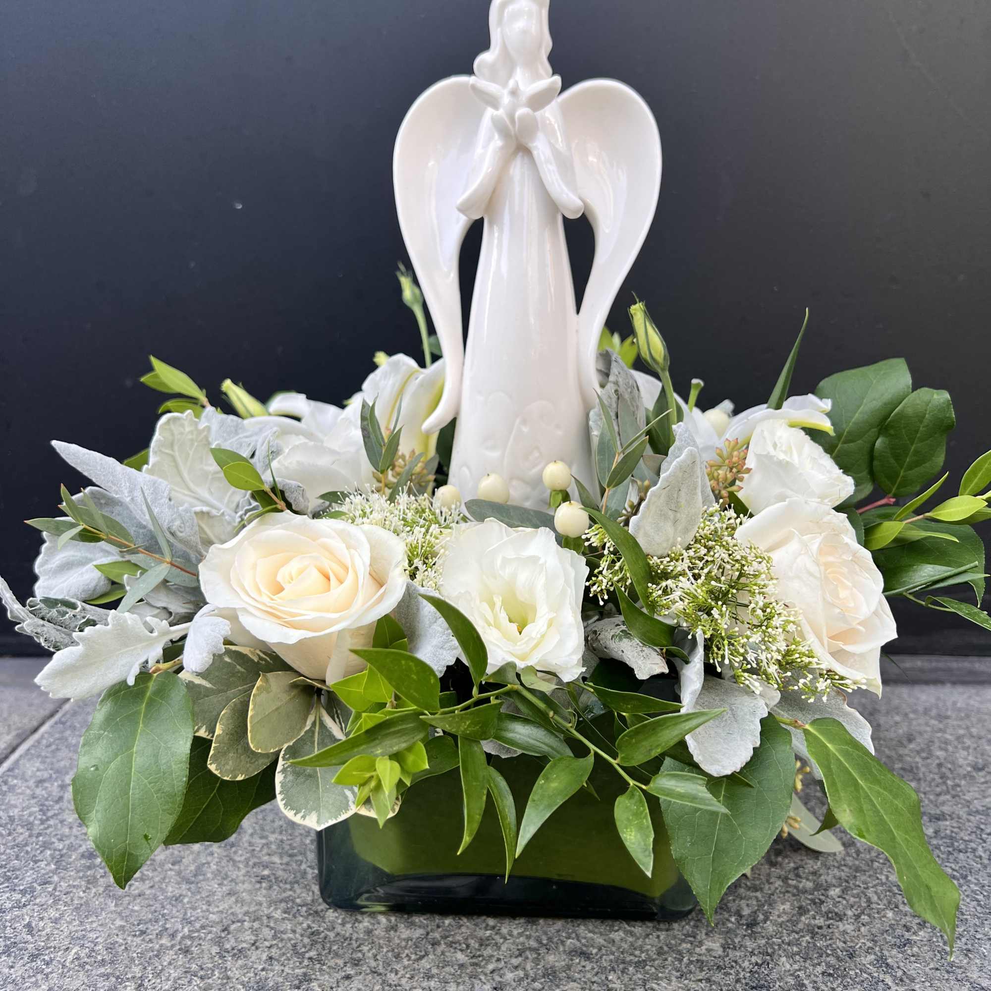White floral arrangement with an angel figurine in a black vase