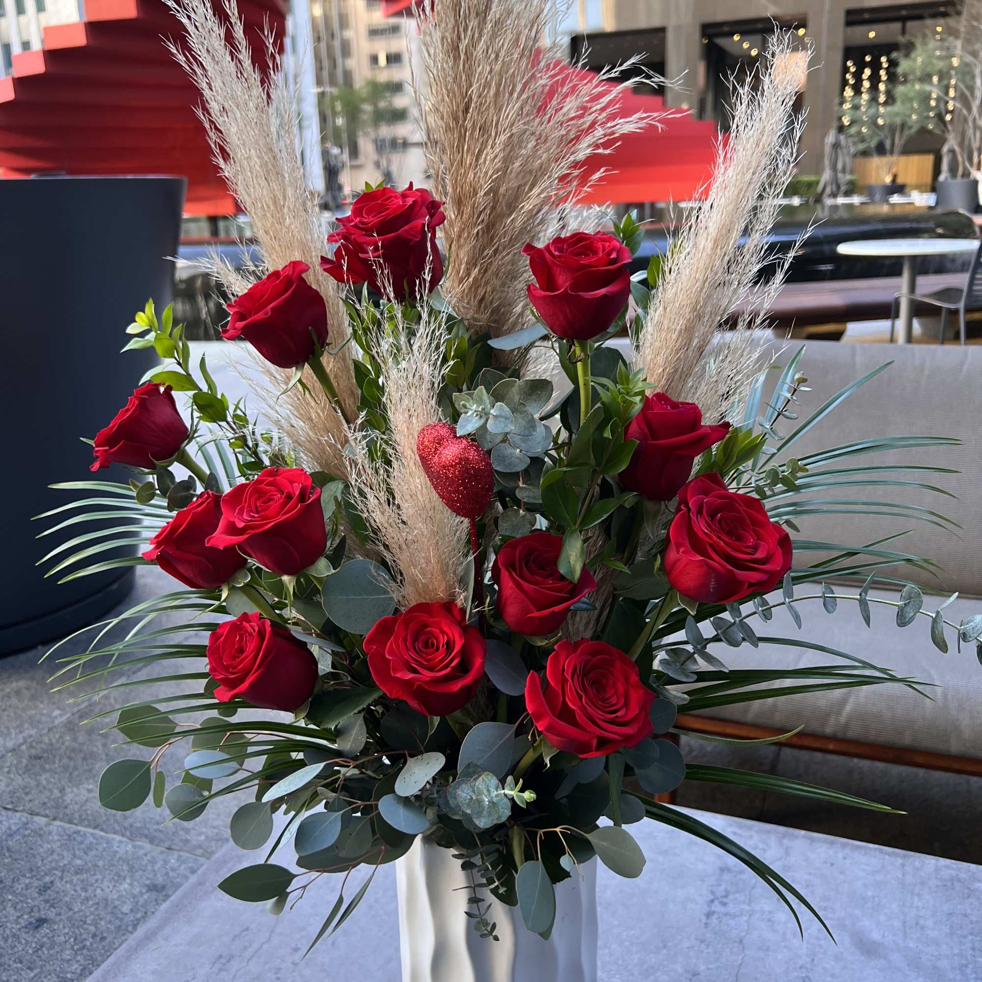 Red roses arranged in a tall white vase with dried grasses and eucalyptus
