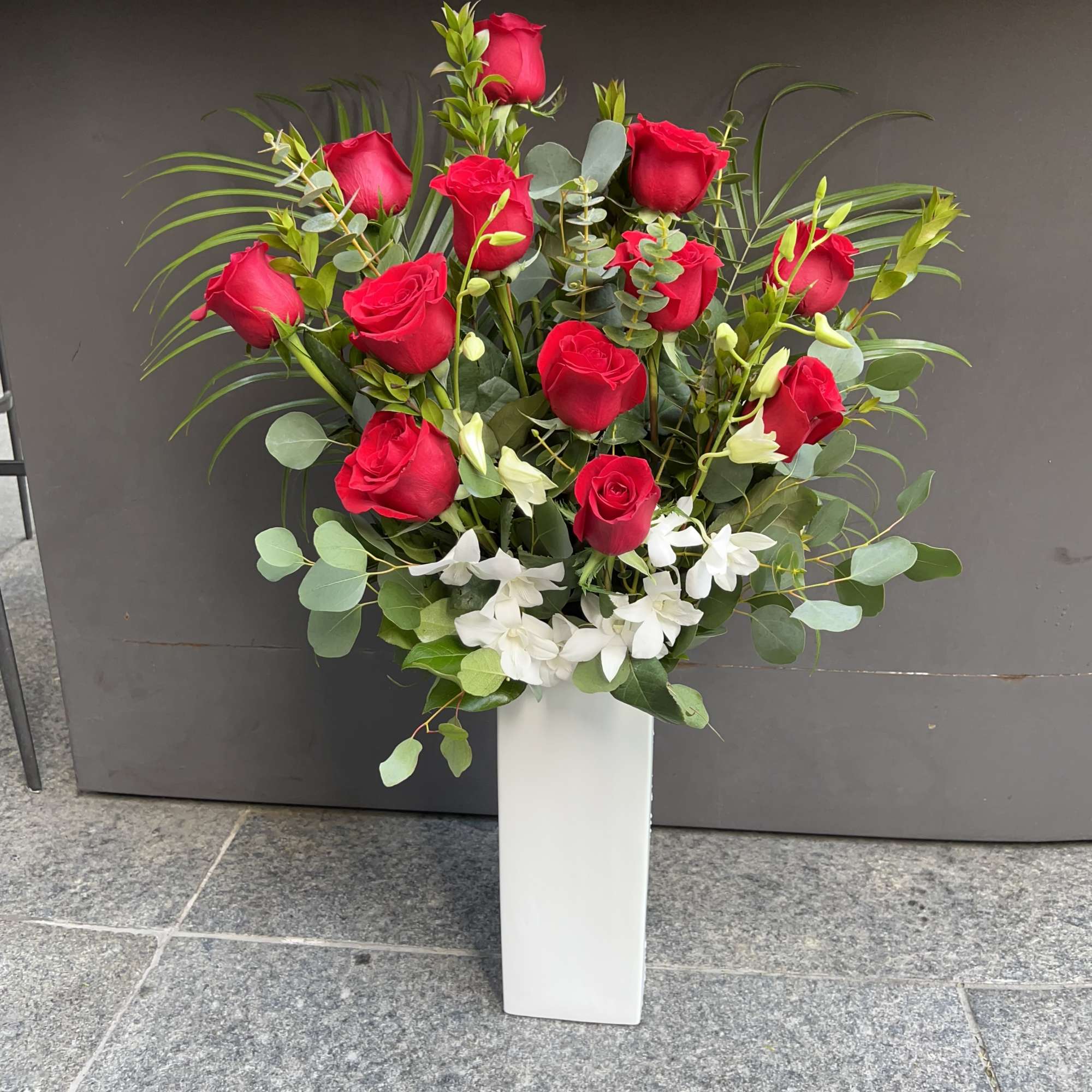 Red roses and white flowers arranged in a tall white vase