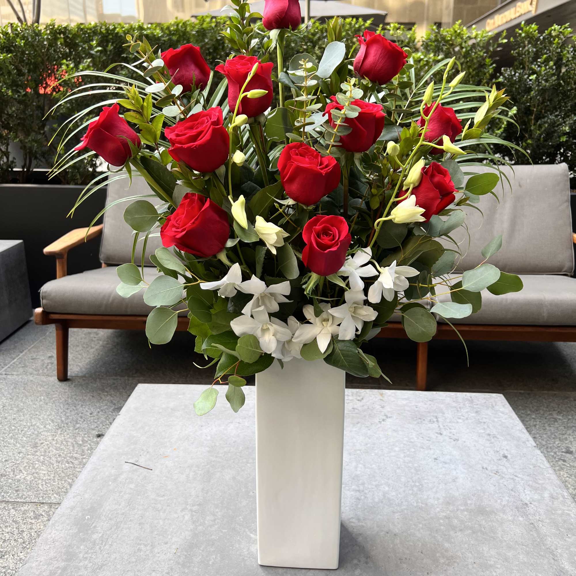Tall arrangement of red roses and white flowers in a white vase