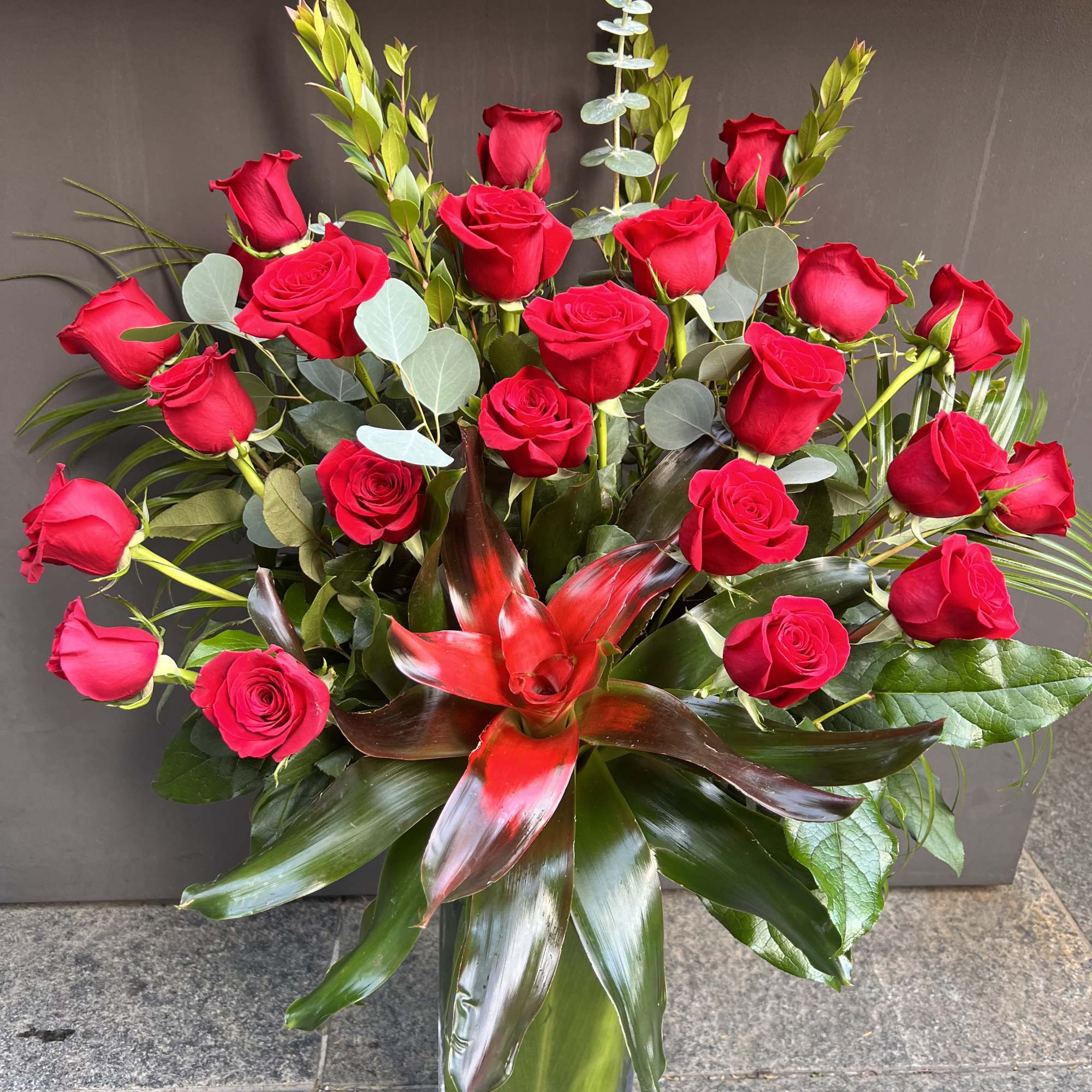 Red roses arranged in a clear glass vase with tropical foliage