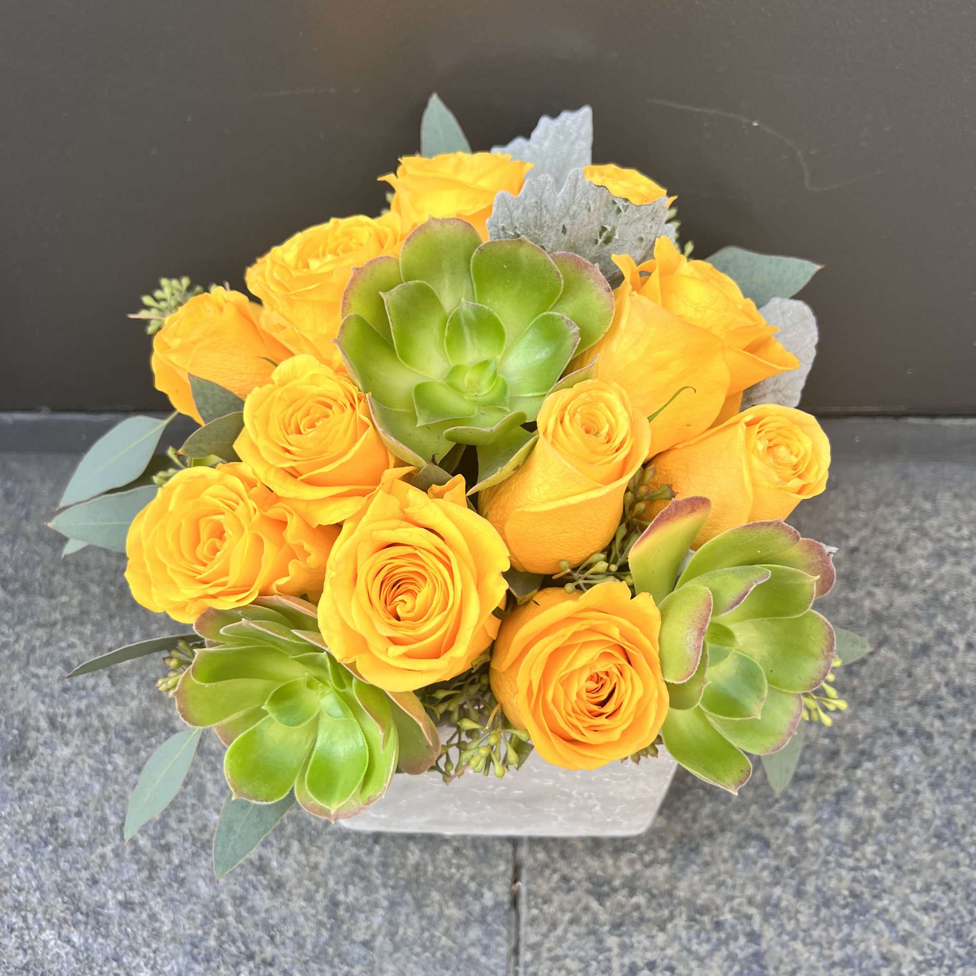 Yellow roses with green succulents in a square vase