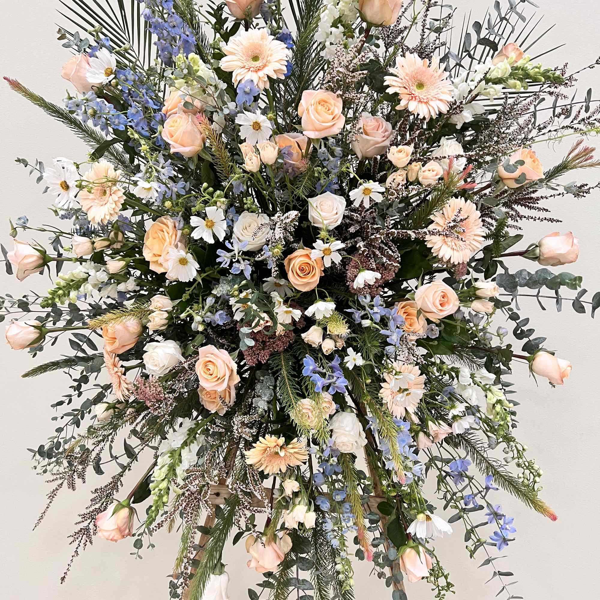 Large standing floral spray with peach roses and blue delphinium