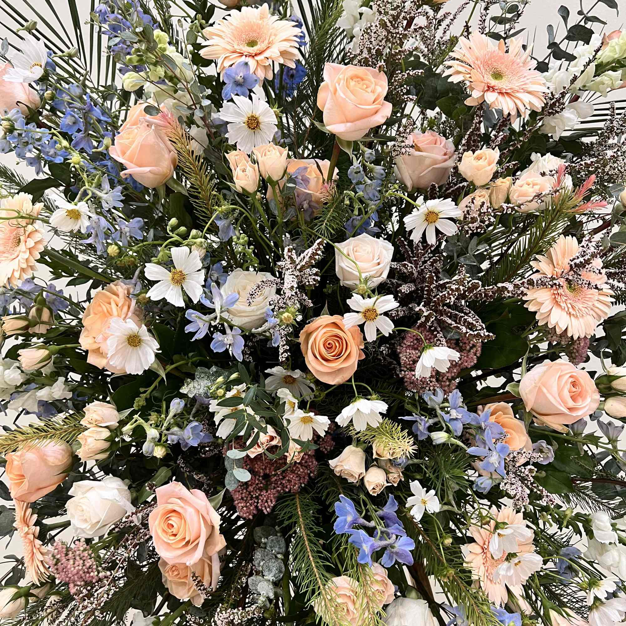 Large pastel floral arrangement with peach roses, white daisies, and blue flowers