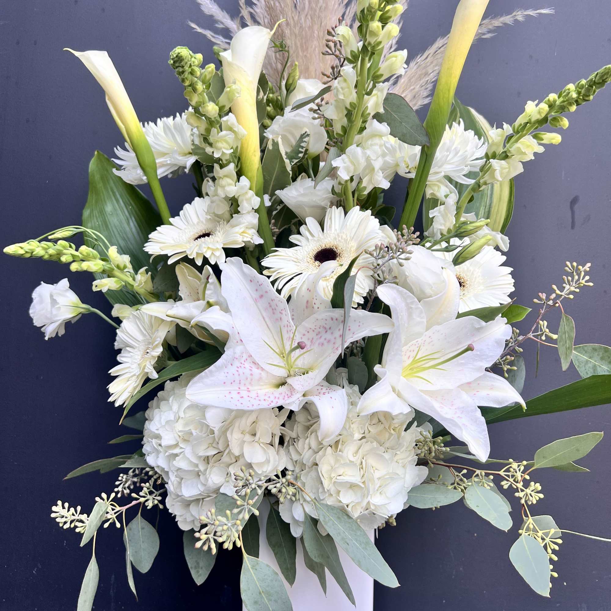 White lilies and gerbera daisies in a tall white vase