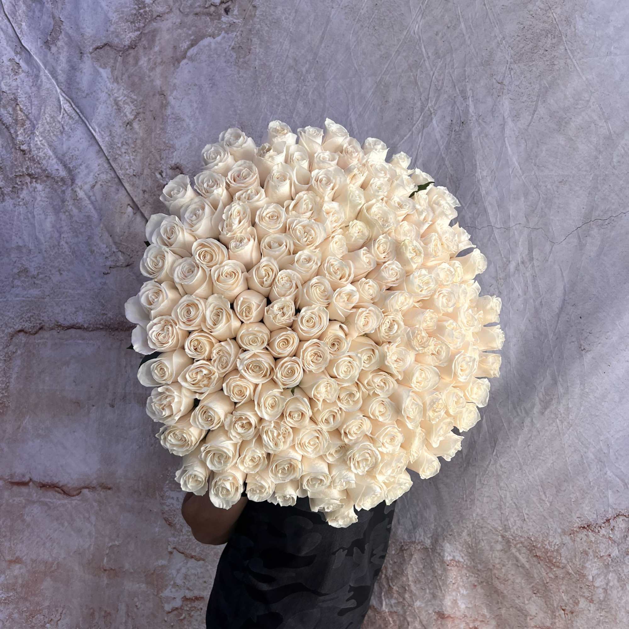 Large bouquet of cream roses held against a textured wall
