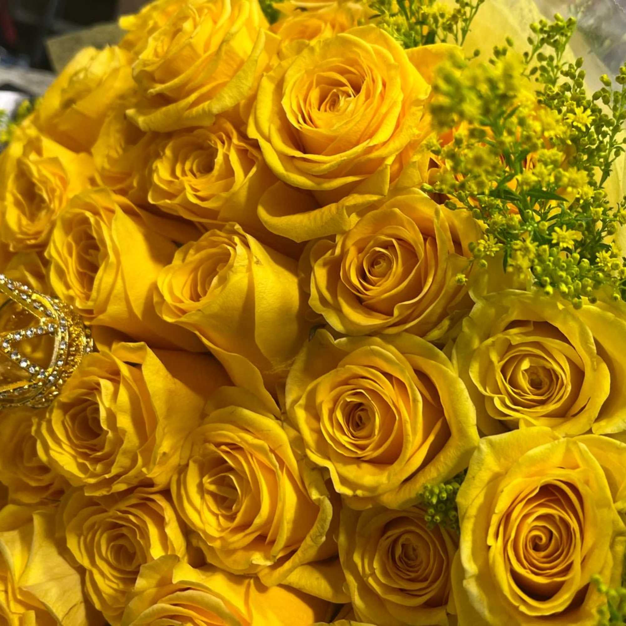 Bouquet of bright yellow roses with small yellow filler flowers and a gold crown accent.