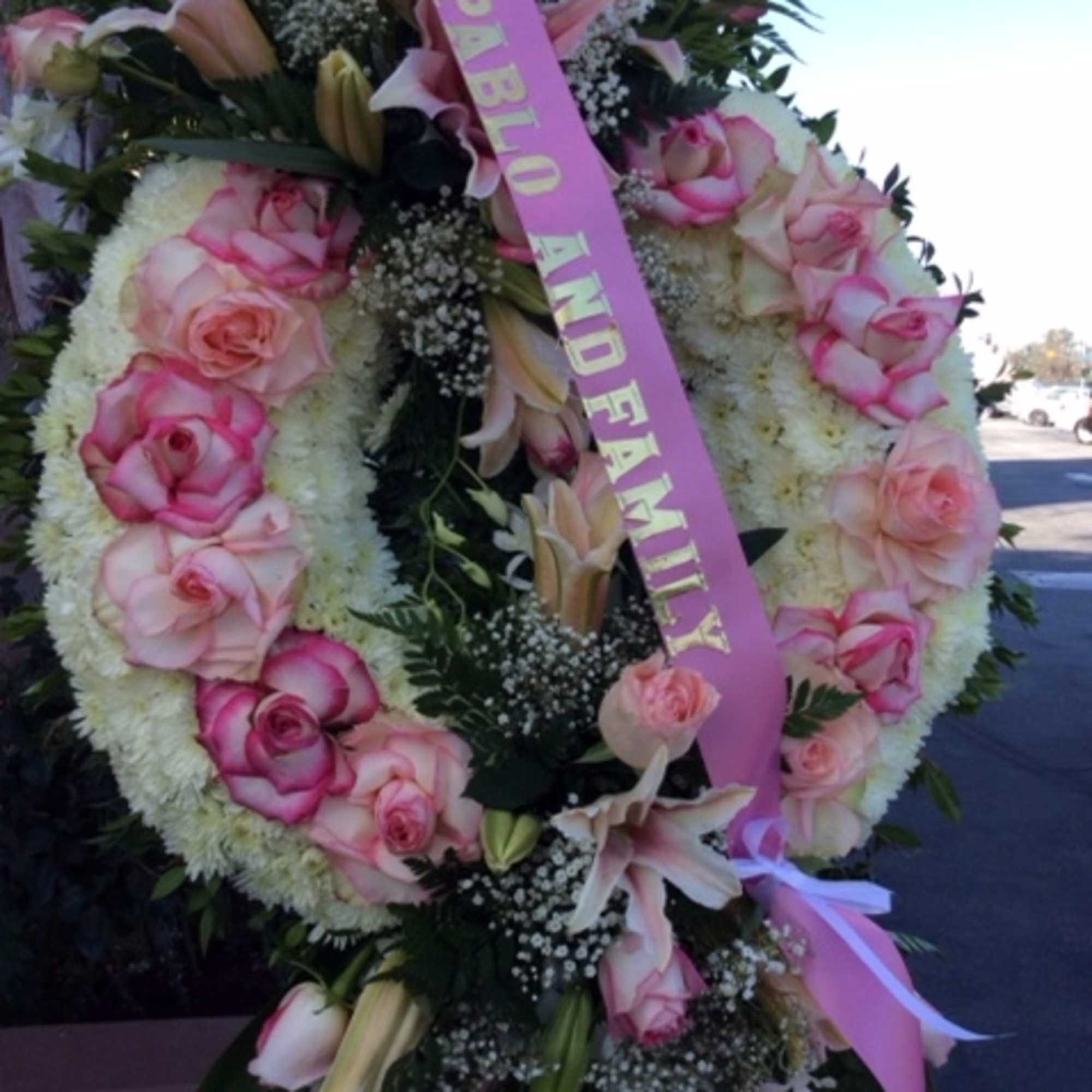 Large floral funeral wreath with pink roses and lilies, accented by a pink ribbon