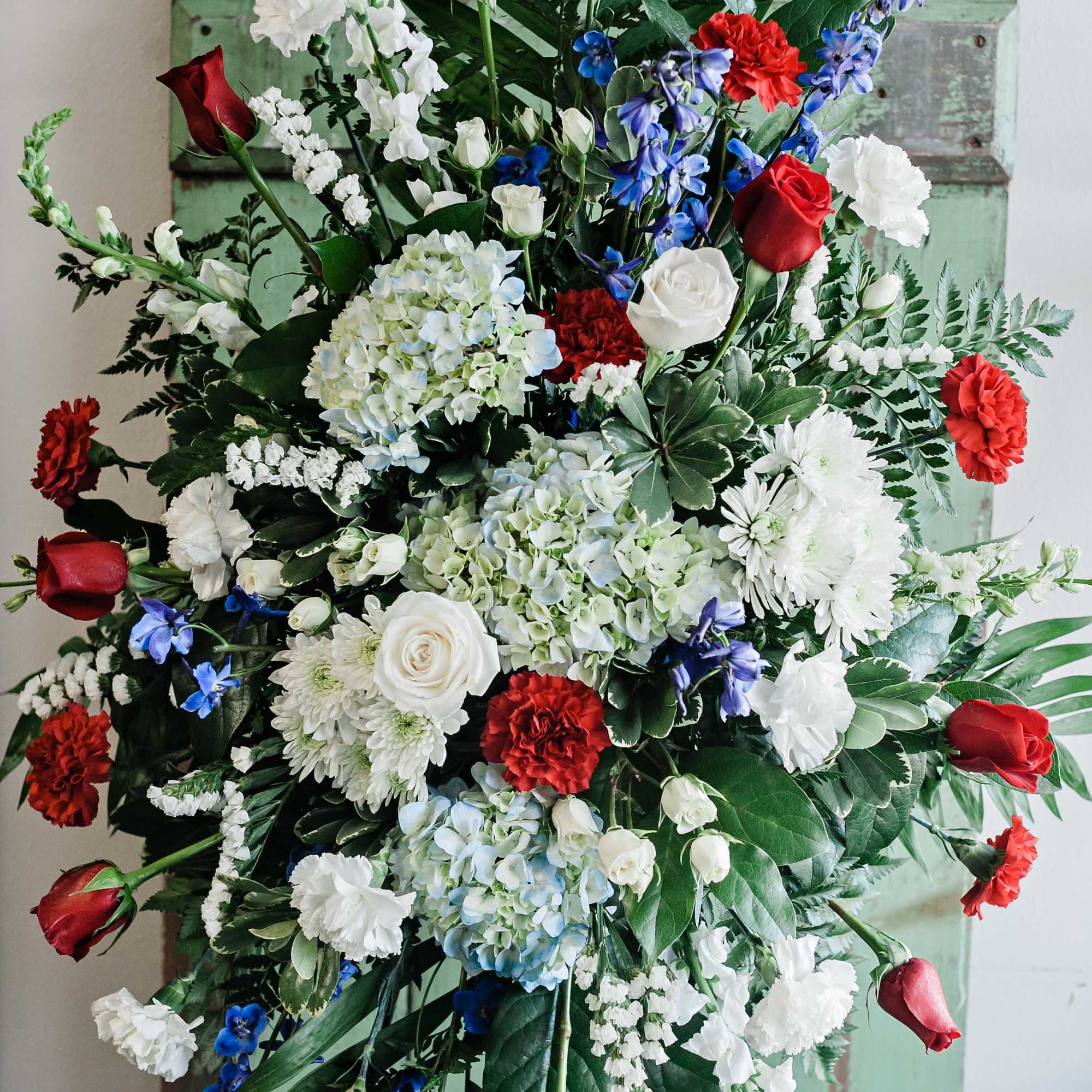 Large standing floral spray with red roses, white blooms, and blue flowers